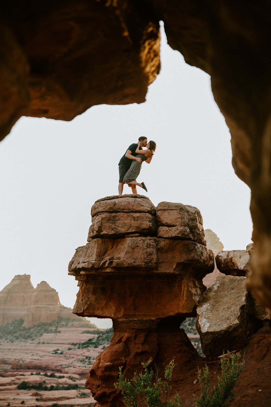 Couple embracing on top of a rock formation framed by a natural arch after they elope to Sedona