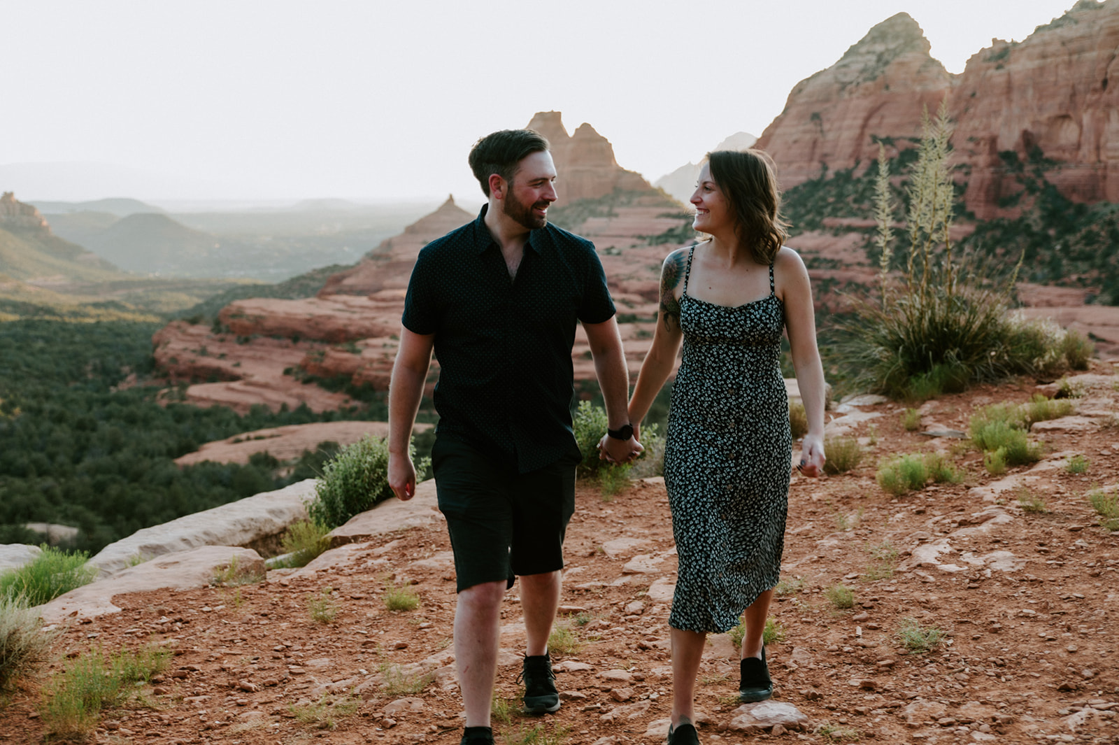Couple walking hand in hand along a red dirt trail with Sedona cliffs in the background
