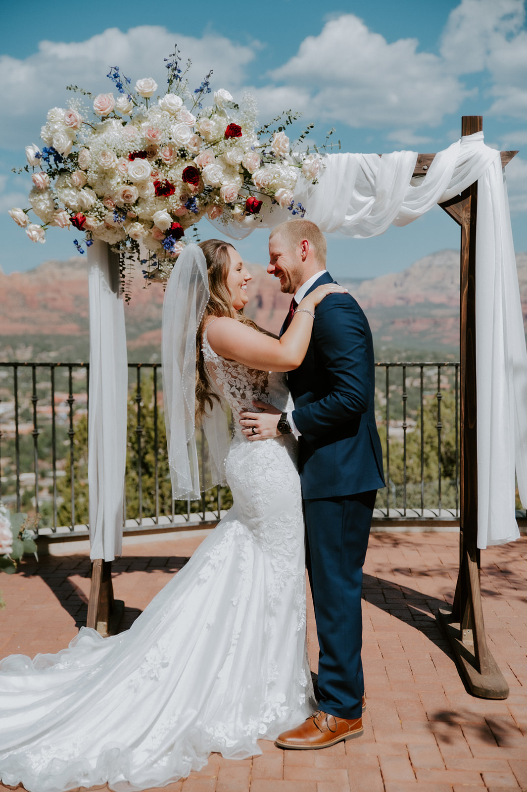 Bride and groom standing under a floral arch during their ceremony after they elope to Sedona
