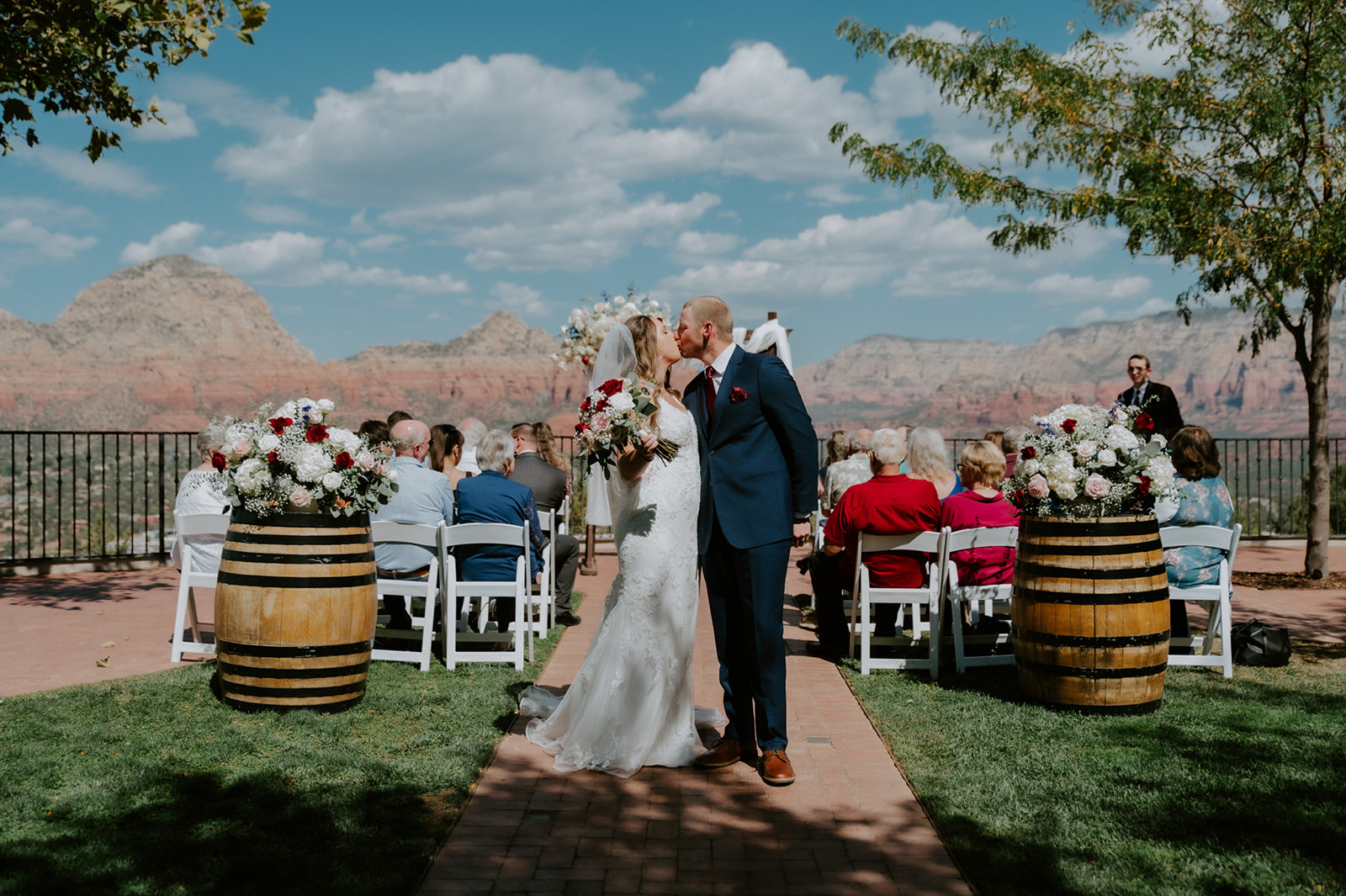 Couple kissing at the end of their ceremony aisle with guests seated and mountain views behind them after they elope to Sedona