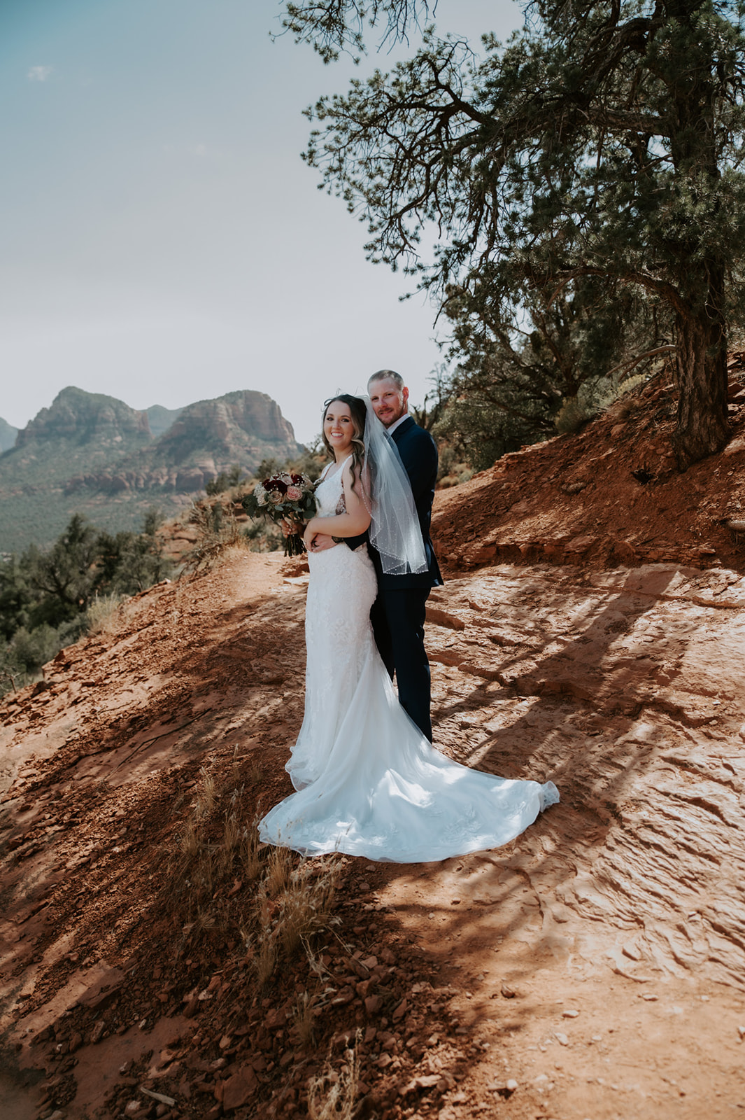 Bride and groom standing together on a red rock trail with sweeping Sedona views after they elope to Sedona