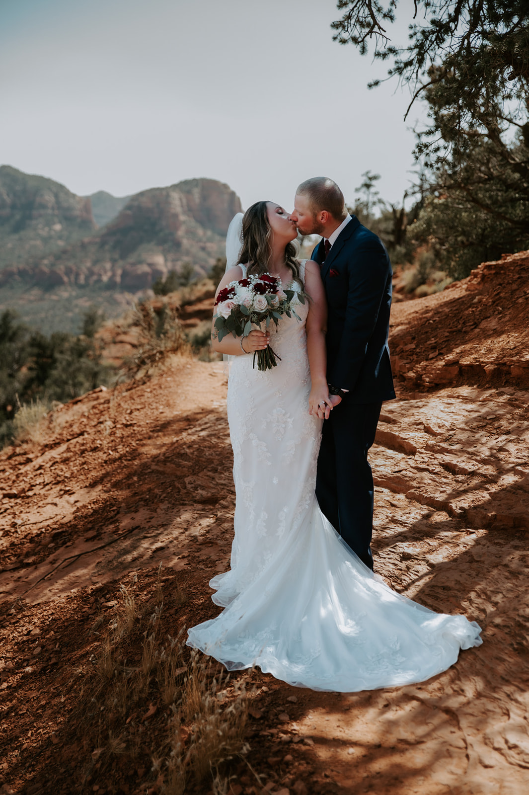 Bride and groom sharing a kiss on a red rock path during their Sedona elopement day