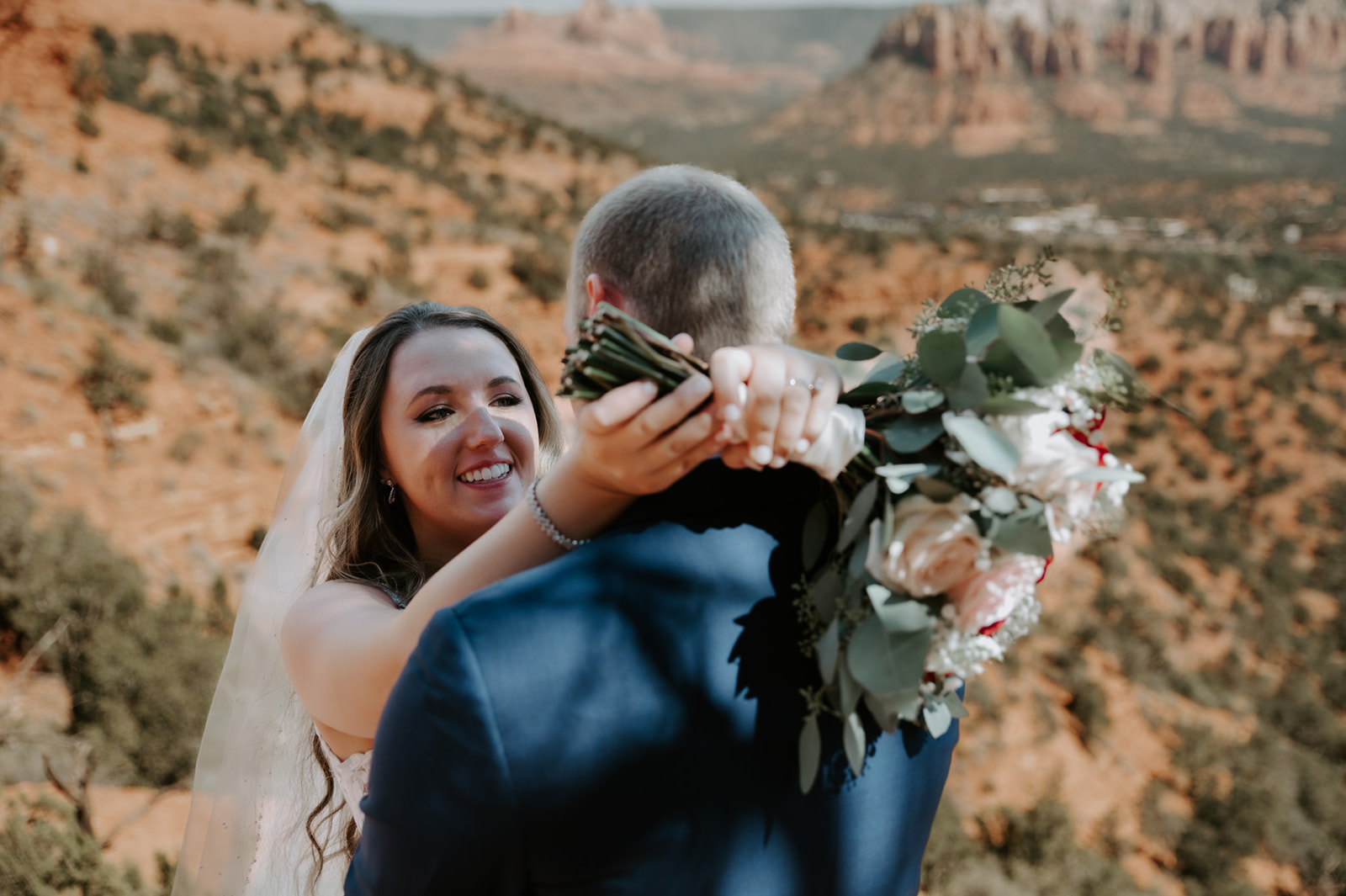 Bride smiling and hugging her partner with a bouquet during their decision to elope to Sedona