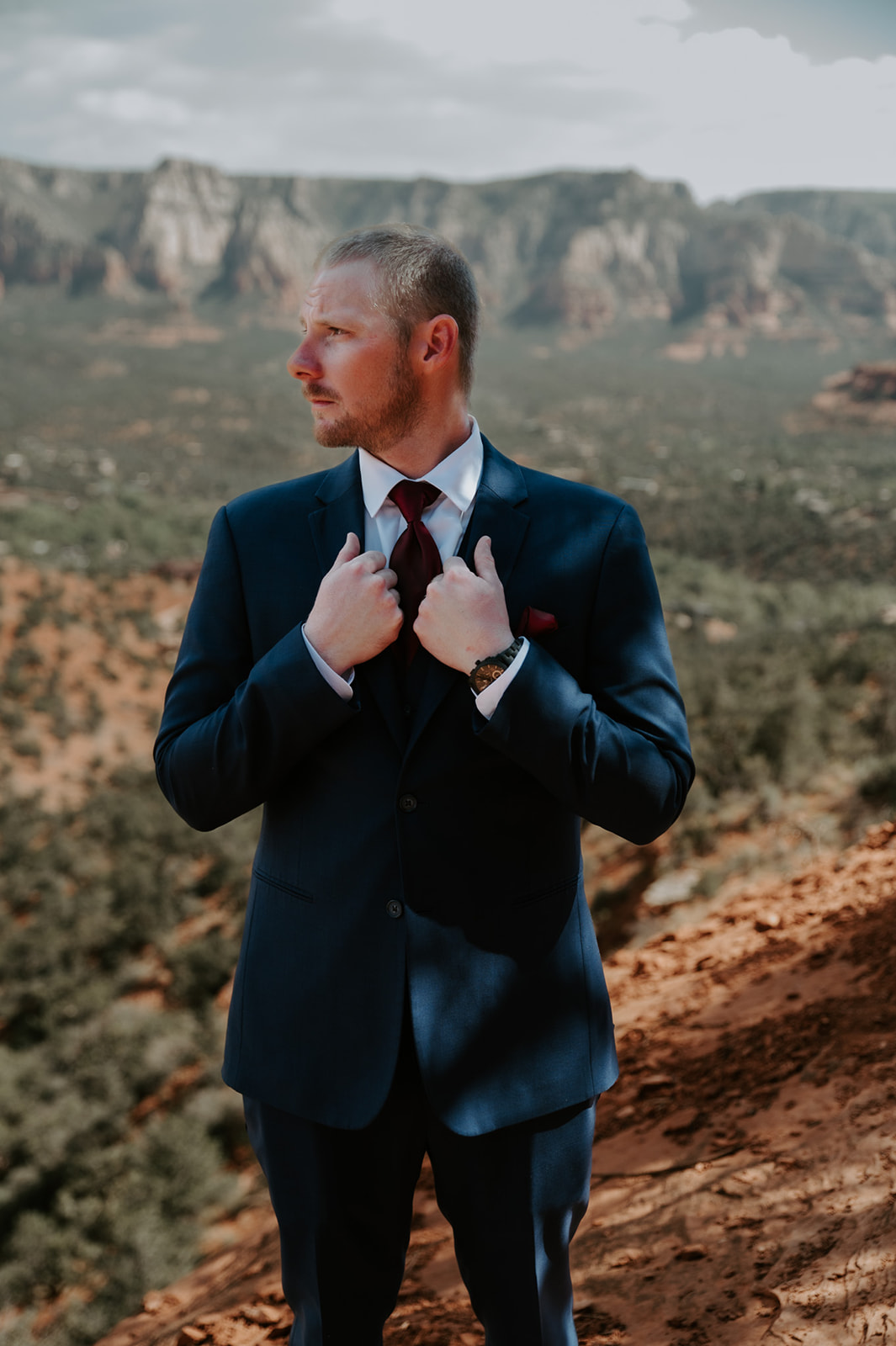 Groom adjusting his suit while standing on a scenic overlook during a Sedona elopement