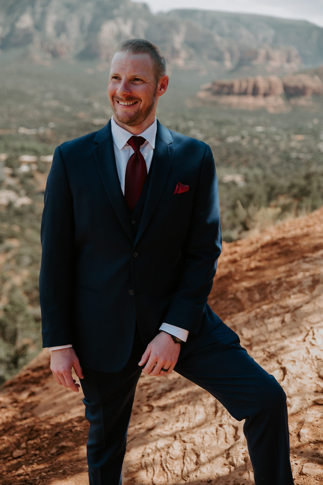 Groom smiling while standing on a red rock overlook during a Sedona elopement