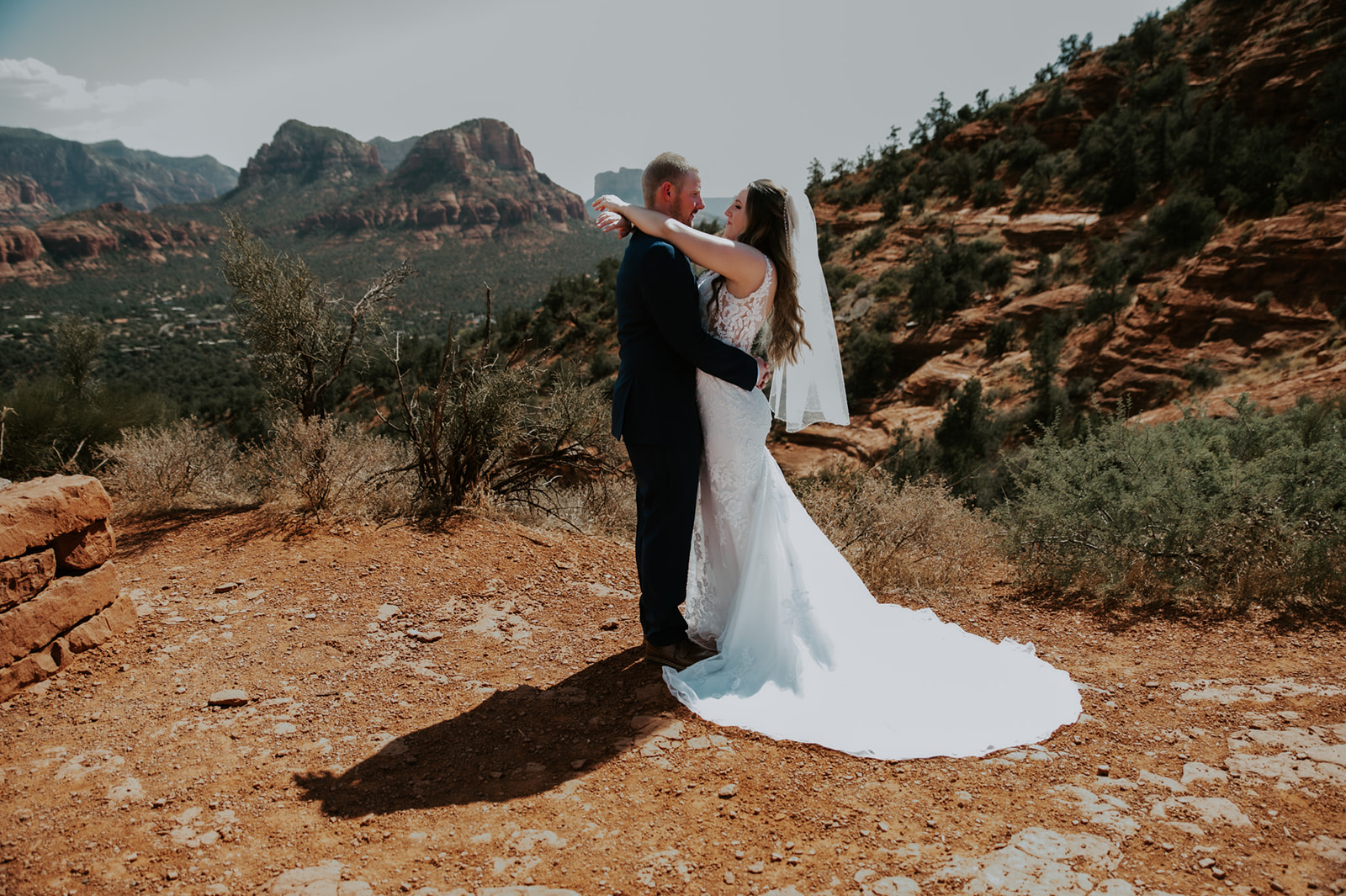 Bride and groom embracing on a cliffside overlook after they elope to Sedona, surrounded by red rock scenery