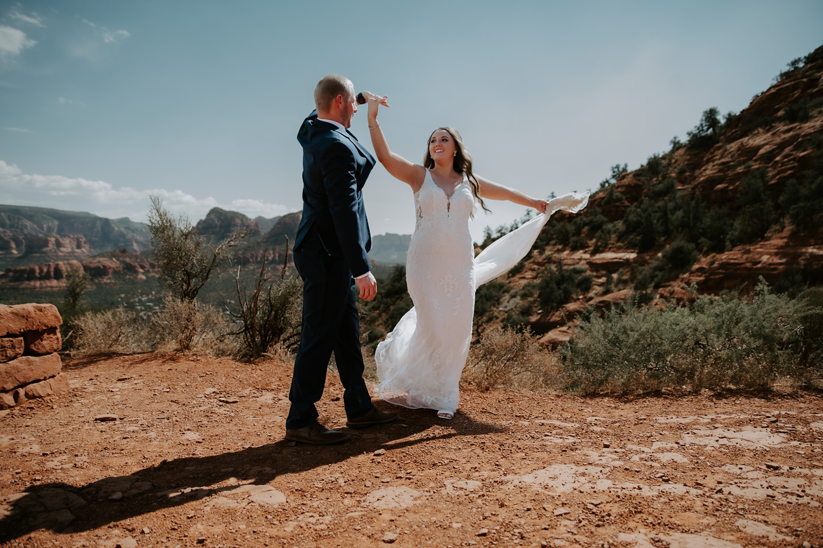 Bride twirling in her dress while holding hands with her partner on a red rock overlook
