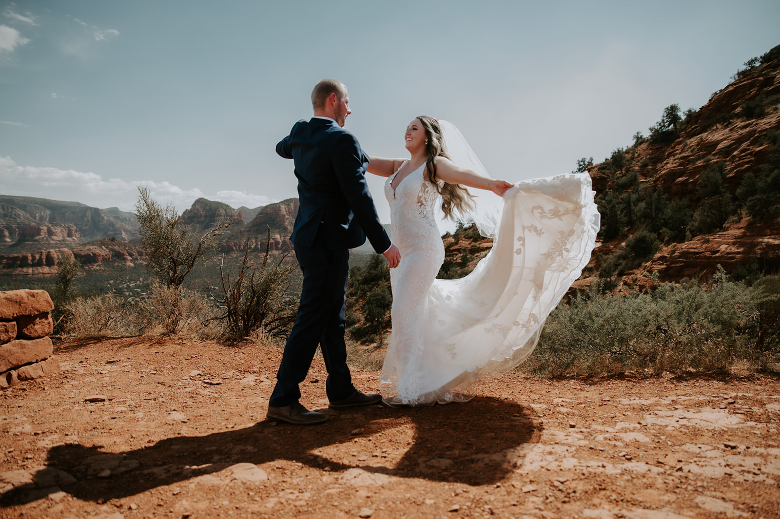 Bride twirling in her dress while holding hands with her partner on a sunlit Sedona trail