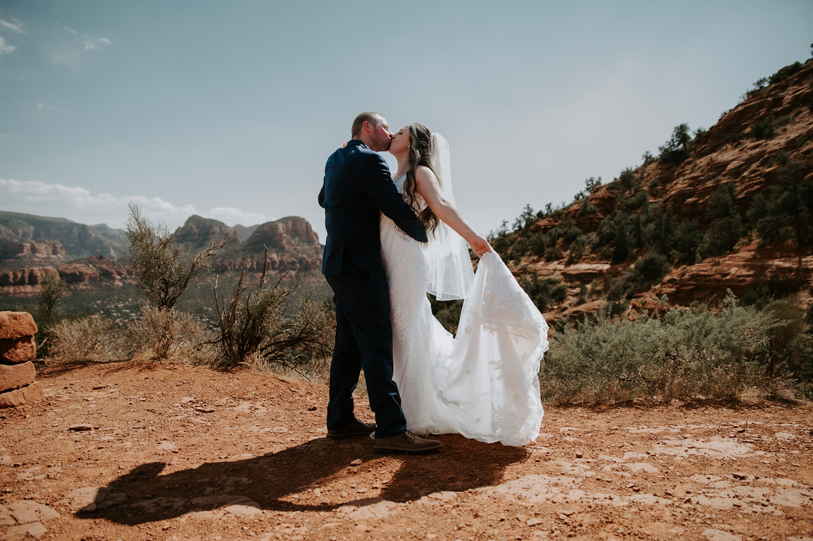 Bride and groom kissing on a red rock overlook with desert mountains behind them during their Sedona elopement