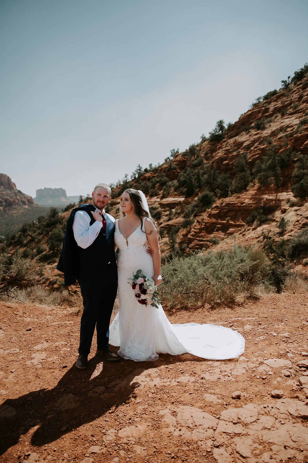 Bride and groom standing together in the desert with red rock cliffs behind them after they elope to Sedona