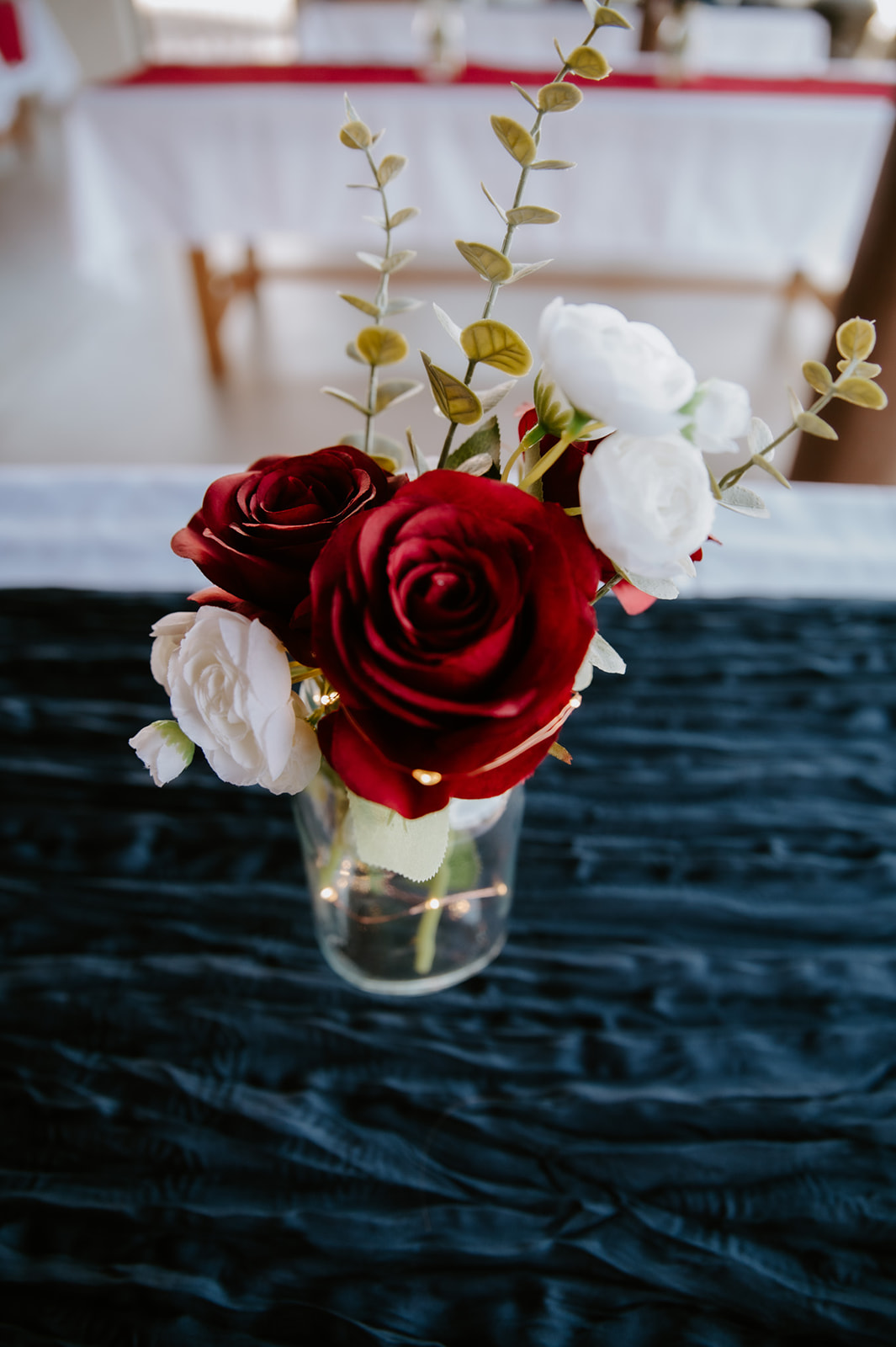 Romantic red and white wedding florals decorating reception tables during an outdoor ceremony