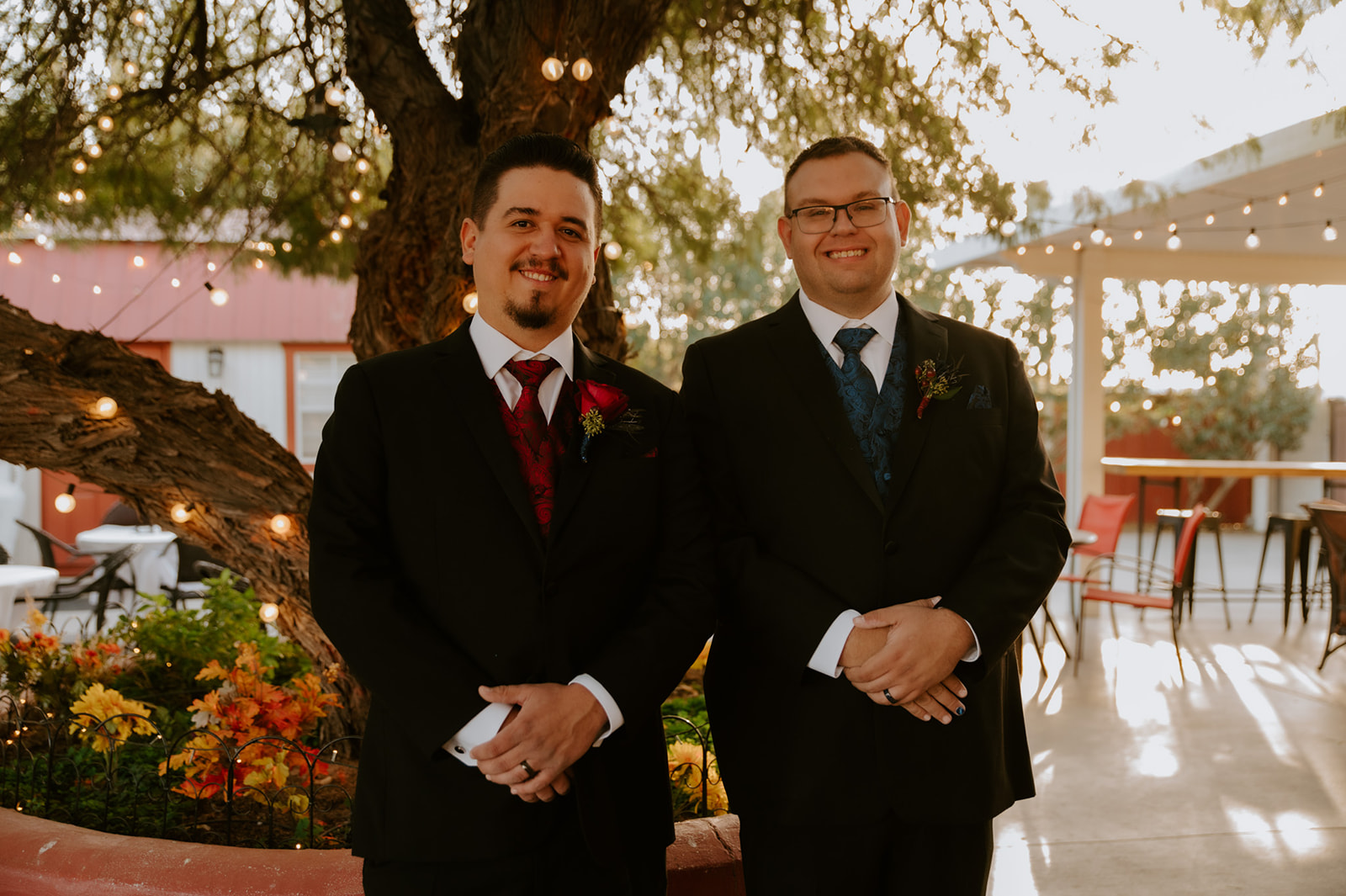 Two grooms smiling together beneath glowing string lights before their ceremony with candid moments captured by an LGBTQ wedding photographer