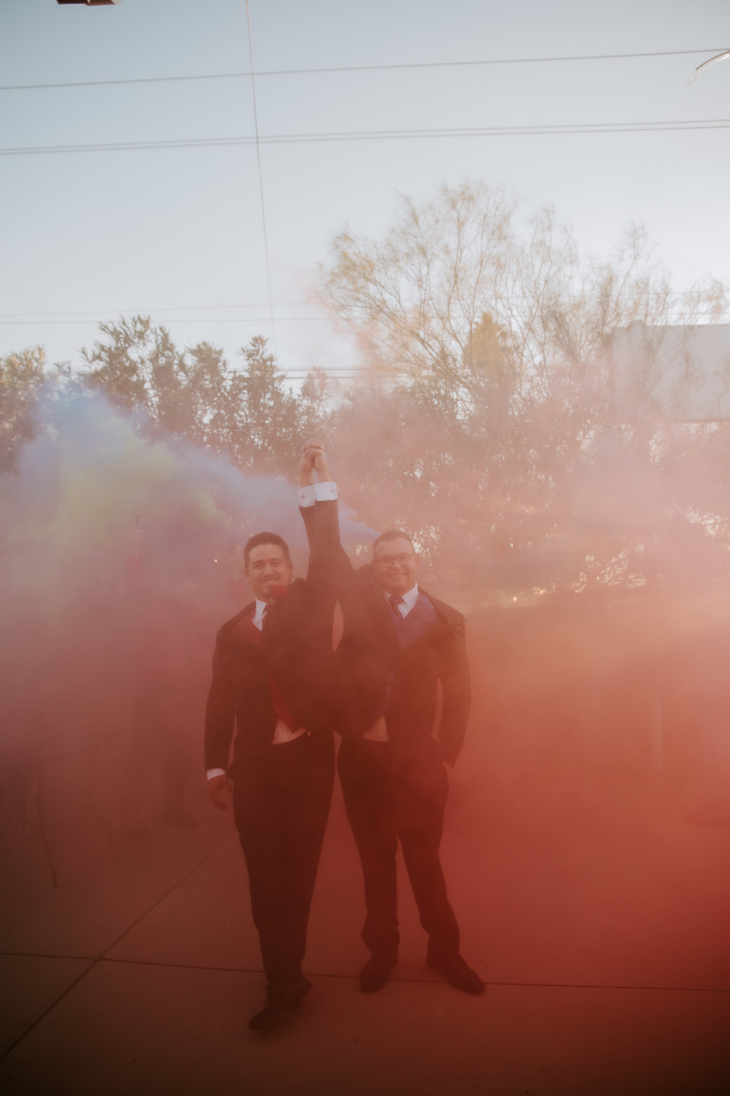 Two grooms celebrating with colorful smoke during an outdoor wedding photographed by an LGBTQ wedding photographer