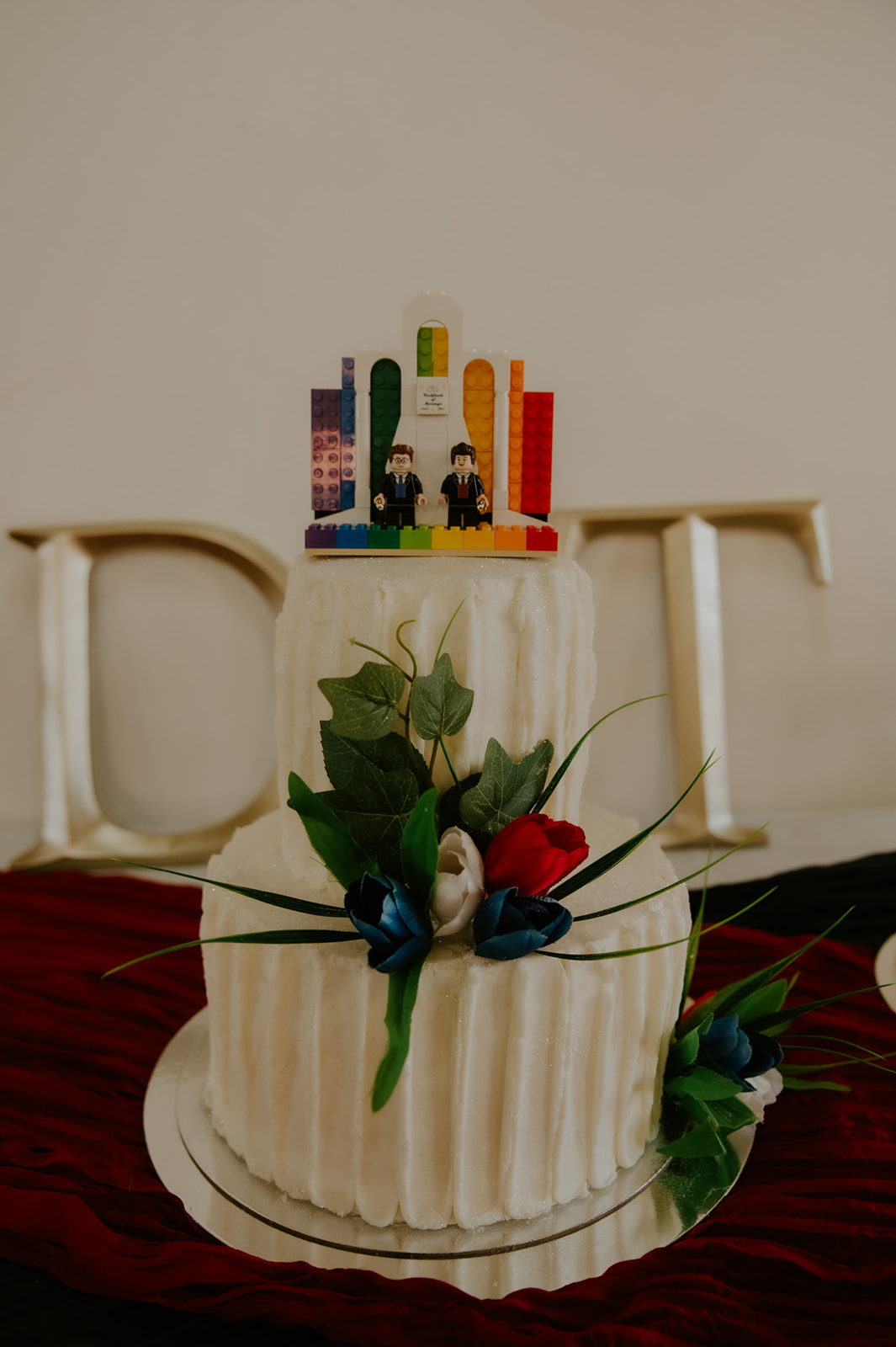 Small wedding cake with rainbow topper and floral details from an LGBTQ wedding photographed by an LGBTQ wedding photographer