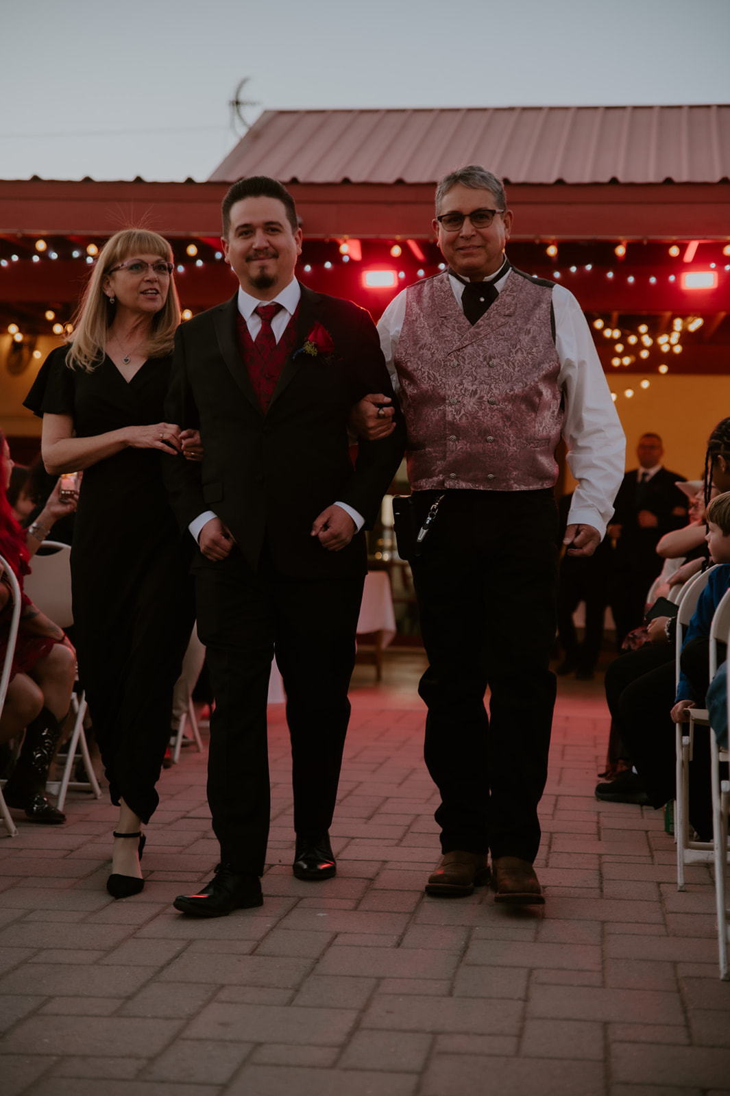 Groom walking down the aisle with family during an emotional wedding ceremony with colorful reception lighting