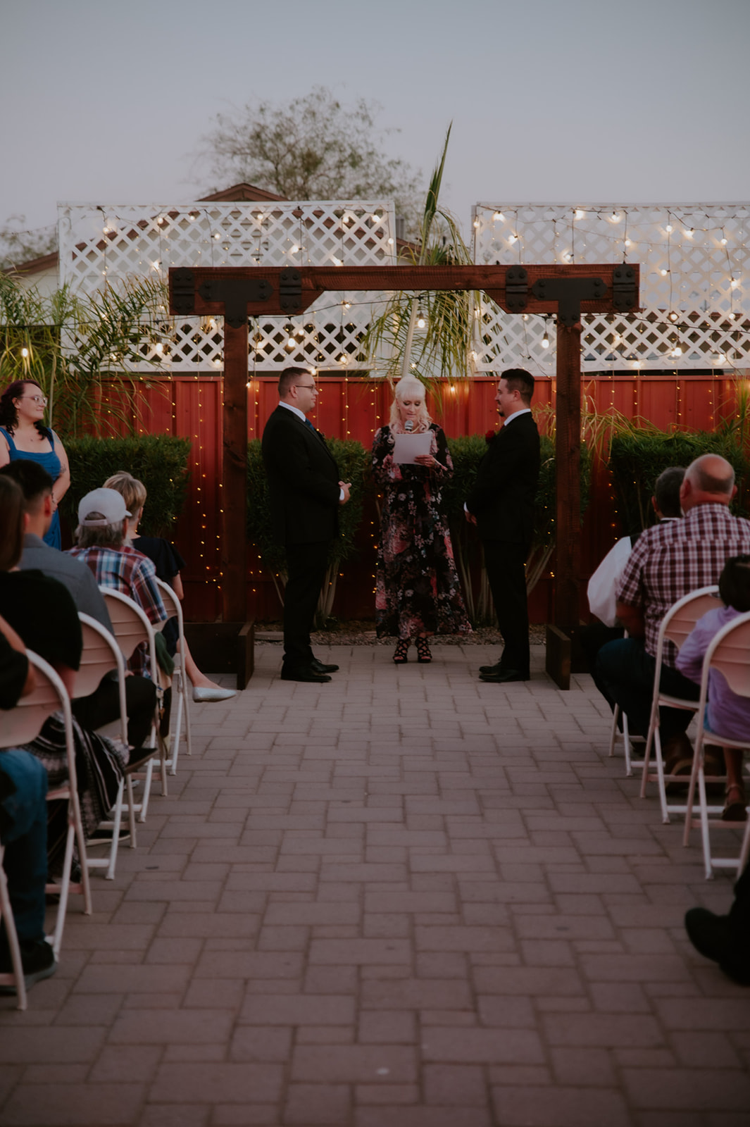 Outdoor ceremony setup for a same-sex wedding with guests gathered around a modern wooden altar at sunset