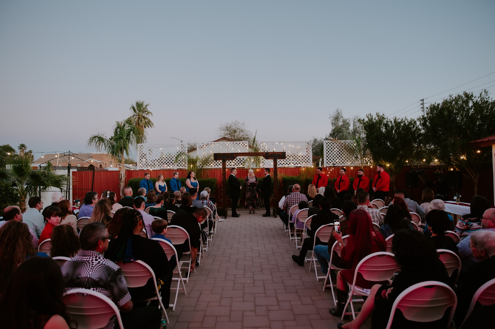 Wide view of an outdoor same-sex wedding ceremony with guests gathered for an emotional evening celebration