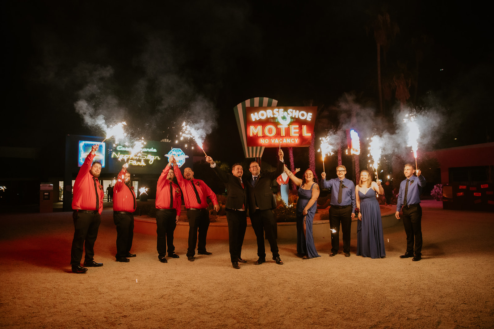 Wedding party holding sparklers outside a retro motel during a fun nighttime celebration photographed by an inclusive wedding photographer