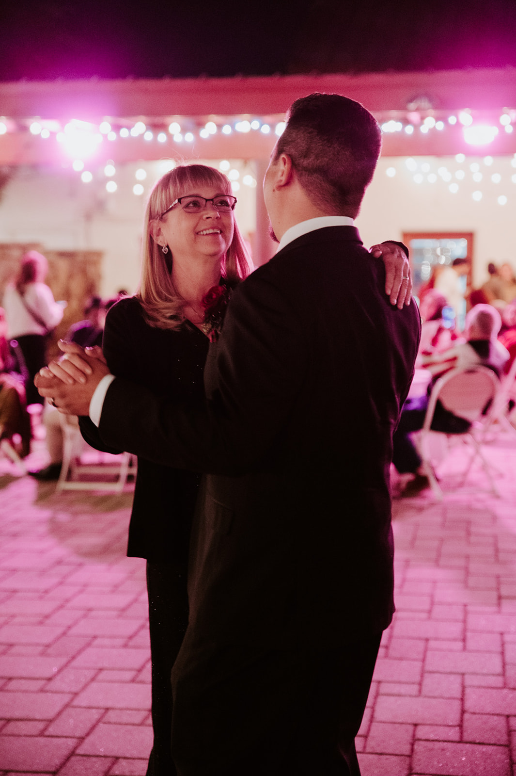 Mother and son dancing together during an emotional wedding reception with pink lighting and candid moments captured by an LGBTQ wedding photographer