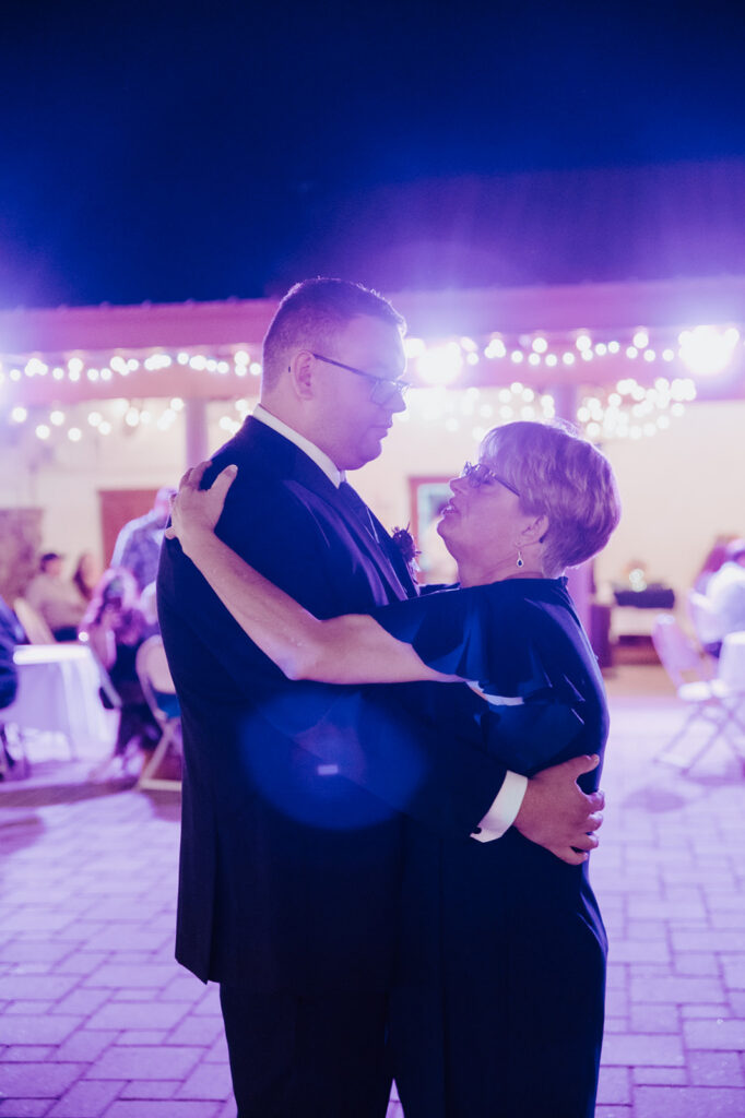 Emotional mother and son dance during a wedding reception photographed by an LGBTQ wedding photographer with vibrant reception lighting