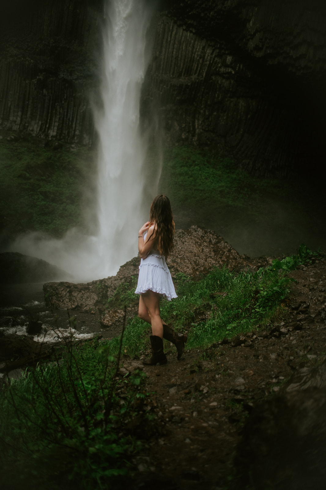 Bride standing beside a dramatic Oregon waterfall surrounded by mist, cliffs, and lush greenery.