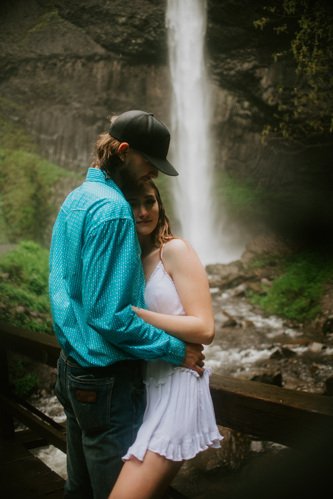 Cozy waterfall portrait with couple embracing on a rainy bridge during an adventurous eloping in Oregon session.