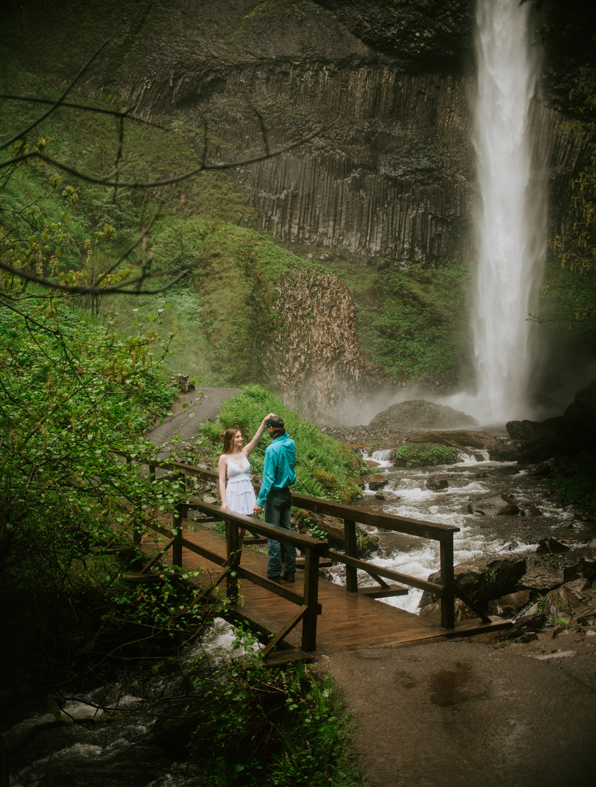 Adventurous couples session beside an Oregon waterfall with lush greenery and rainy forest scenery.