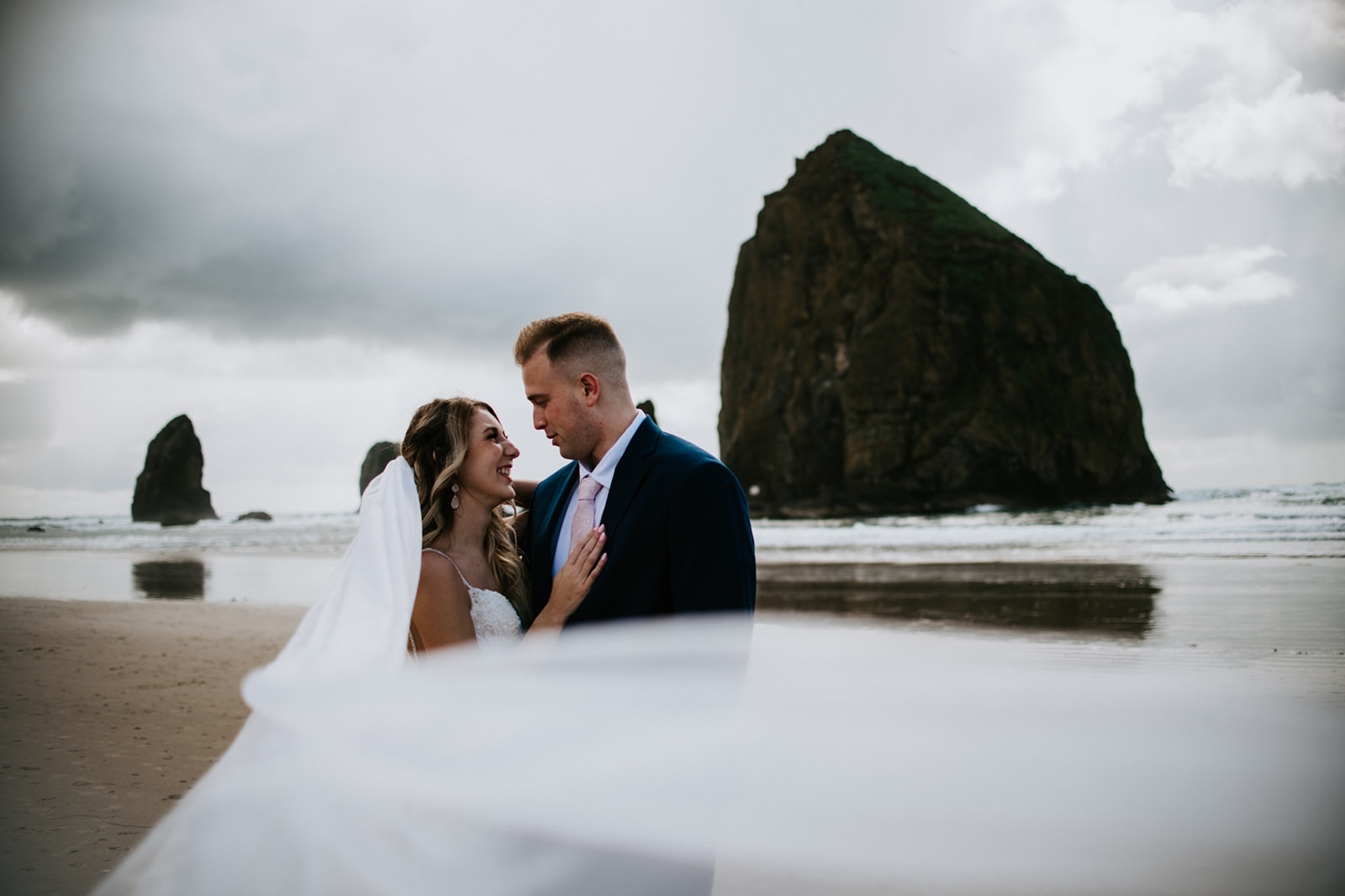 Windy Oregon Coast elopement portrait with flowing veil and Haystack Rock in the background.