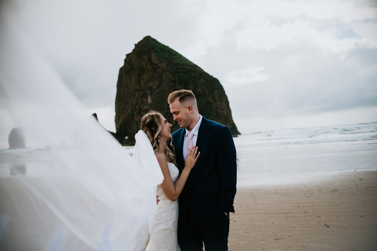 Romantic Cannon Beach elopement portrait with flowing veil and dramatic Oregon coastline scenery.