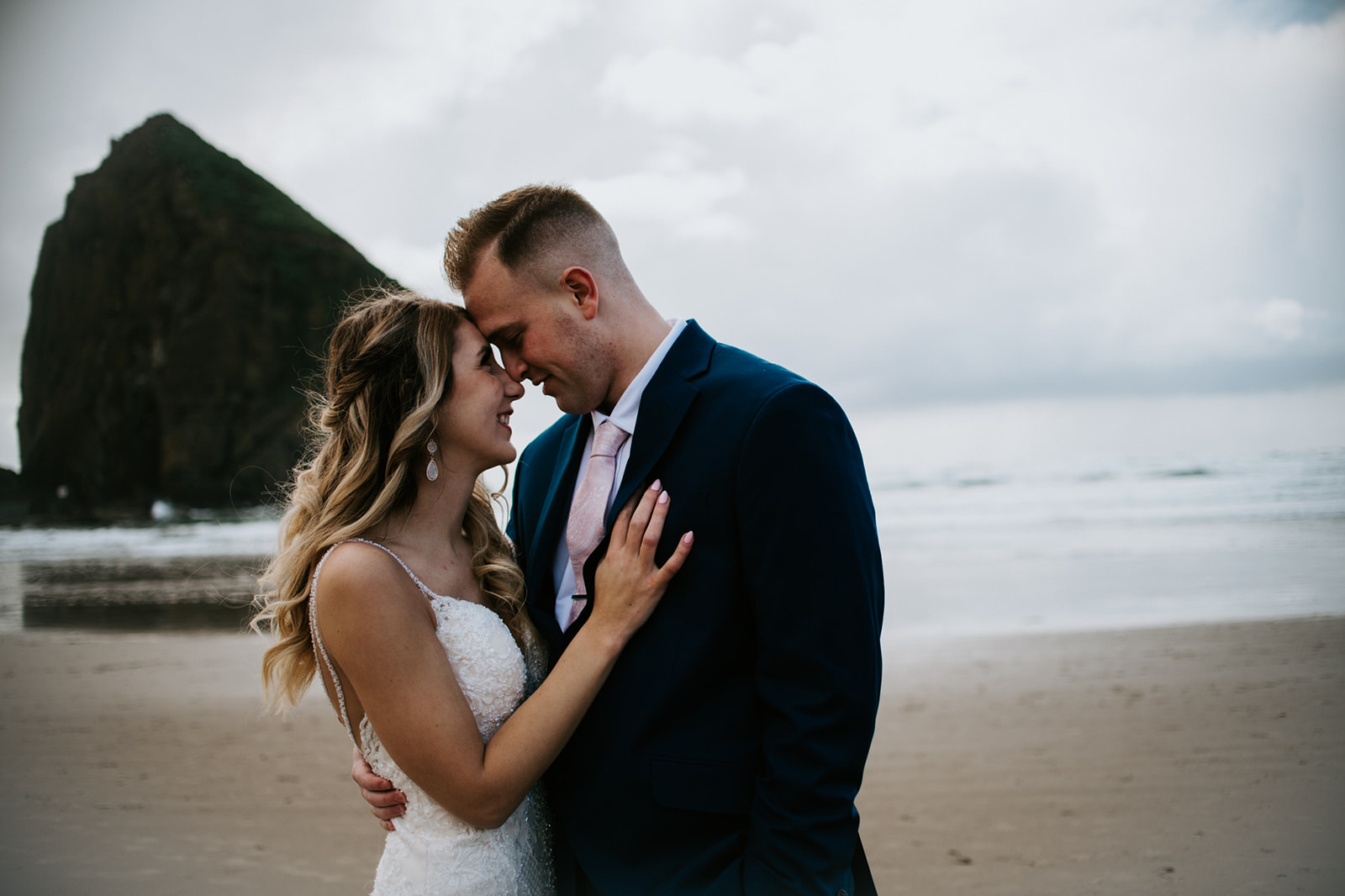 Romantic beach portrait with bride and groom embracing beside Haystack Rock on the Oregon Coast.