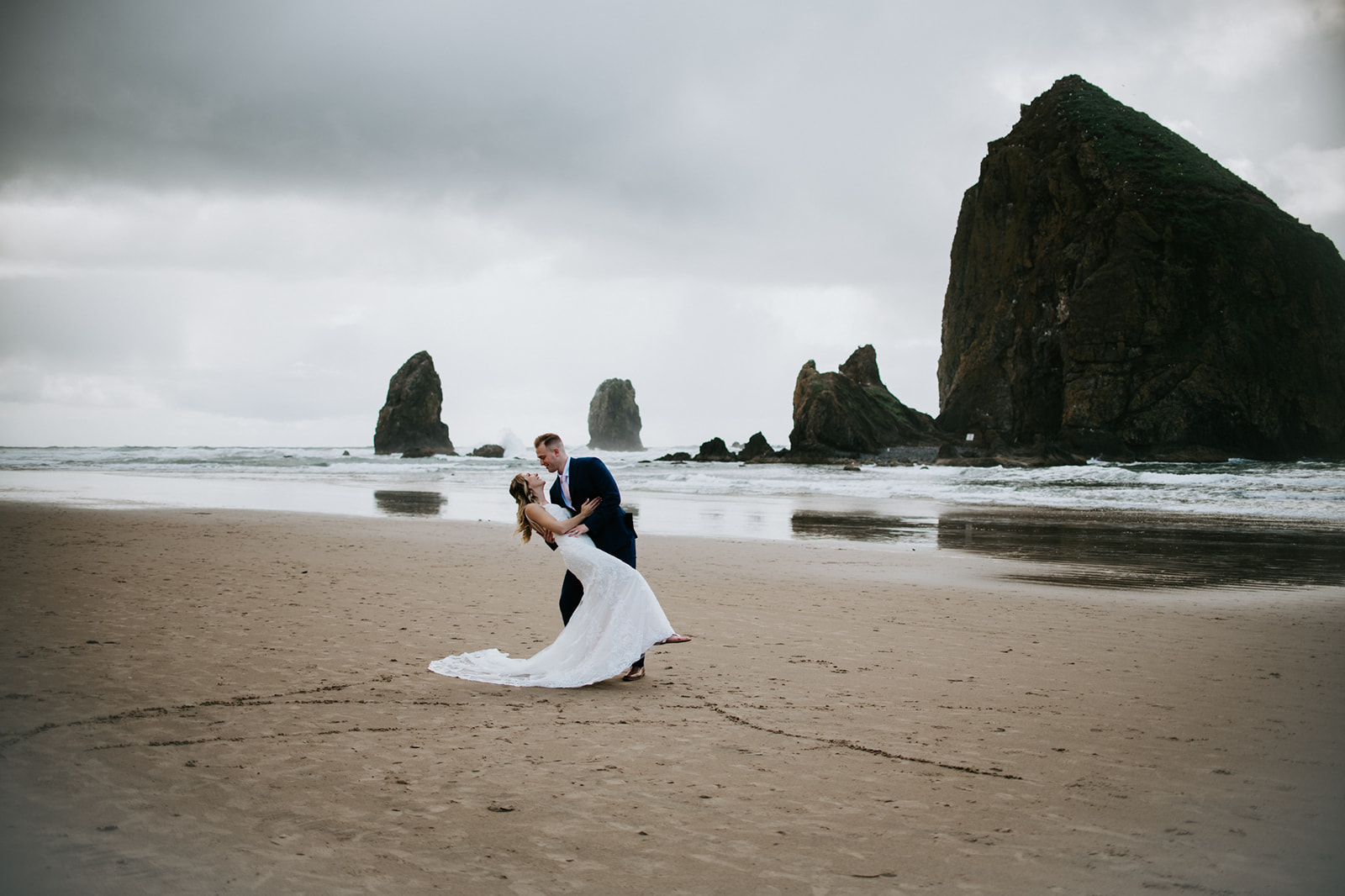 Bride and groom dipping on the Oregon Coast during a moody beach elopement portrait session.