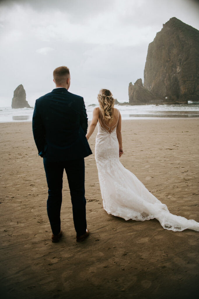 Bride and groom walking toward Haystack Rock during a romantic eloping in Oregon experience on the coast.