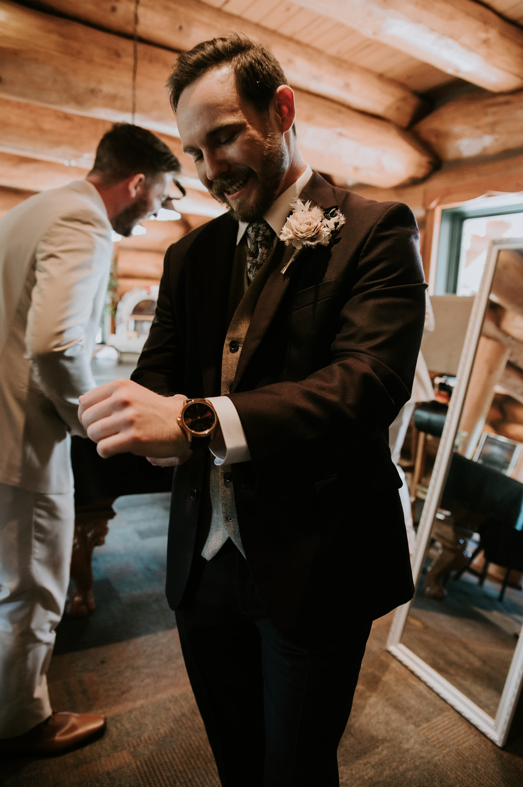 Groom smiles while checking his watch as he gets dressed alongside his groomsmen.
