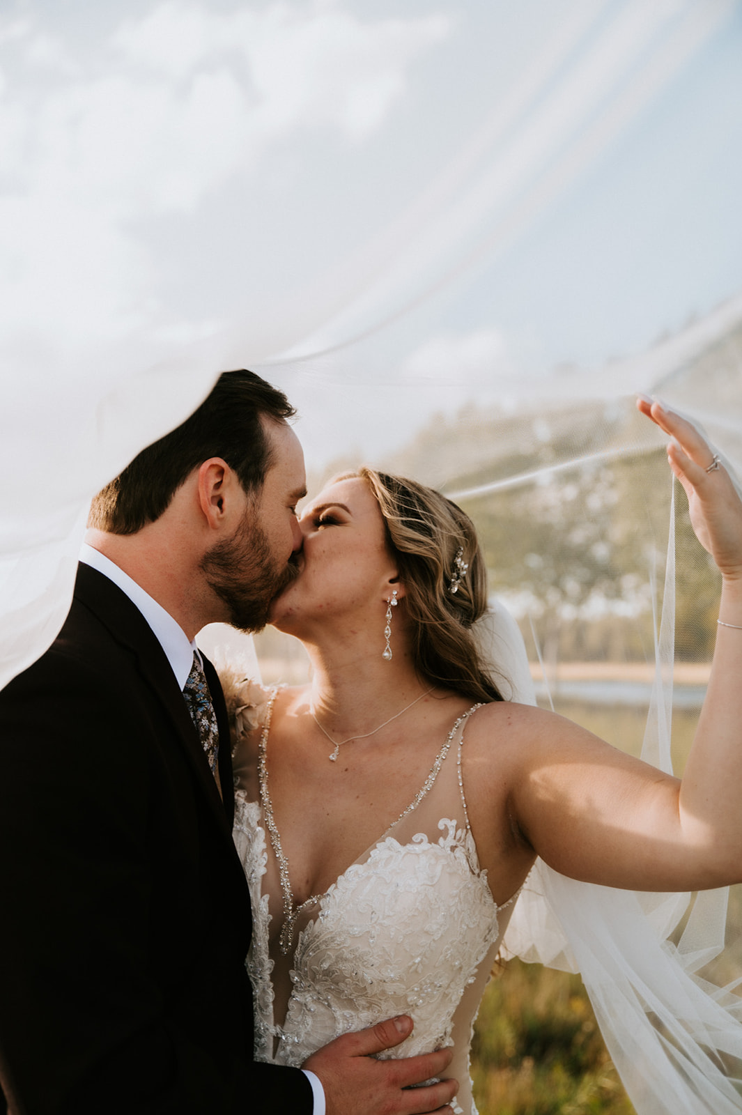 Bride and groom share a kiss beneath a flowing veil, a romantic wedding portrait that inspires couples planning an elopement.
