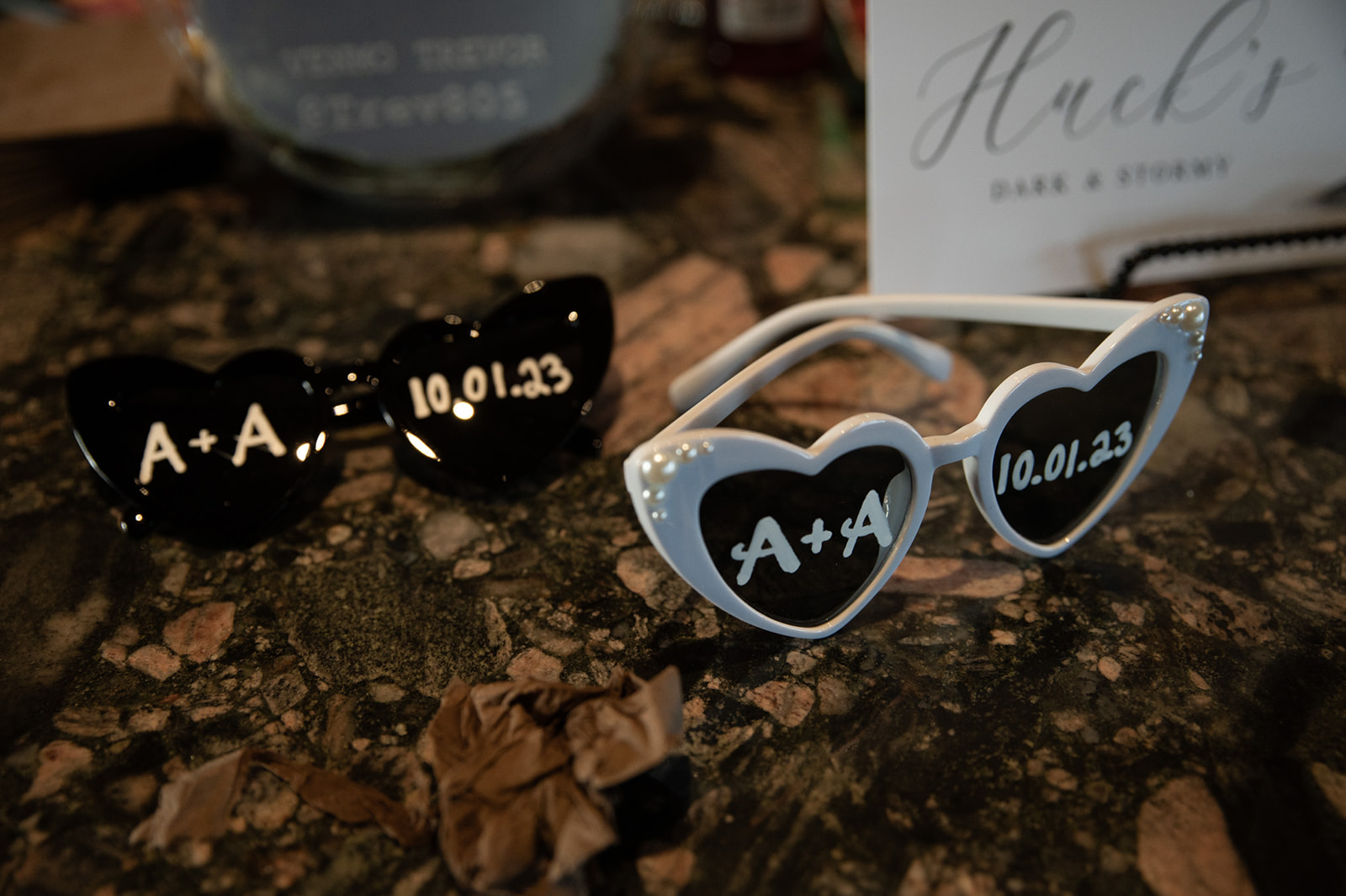 Personalized heart-shaped wedding sunglasses displayed on a reception table with custom wedding details.
