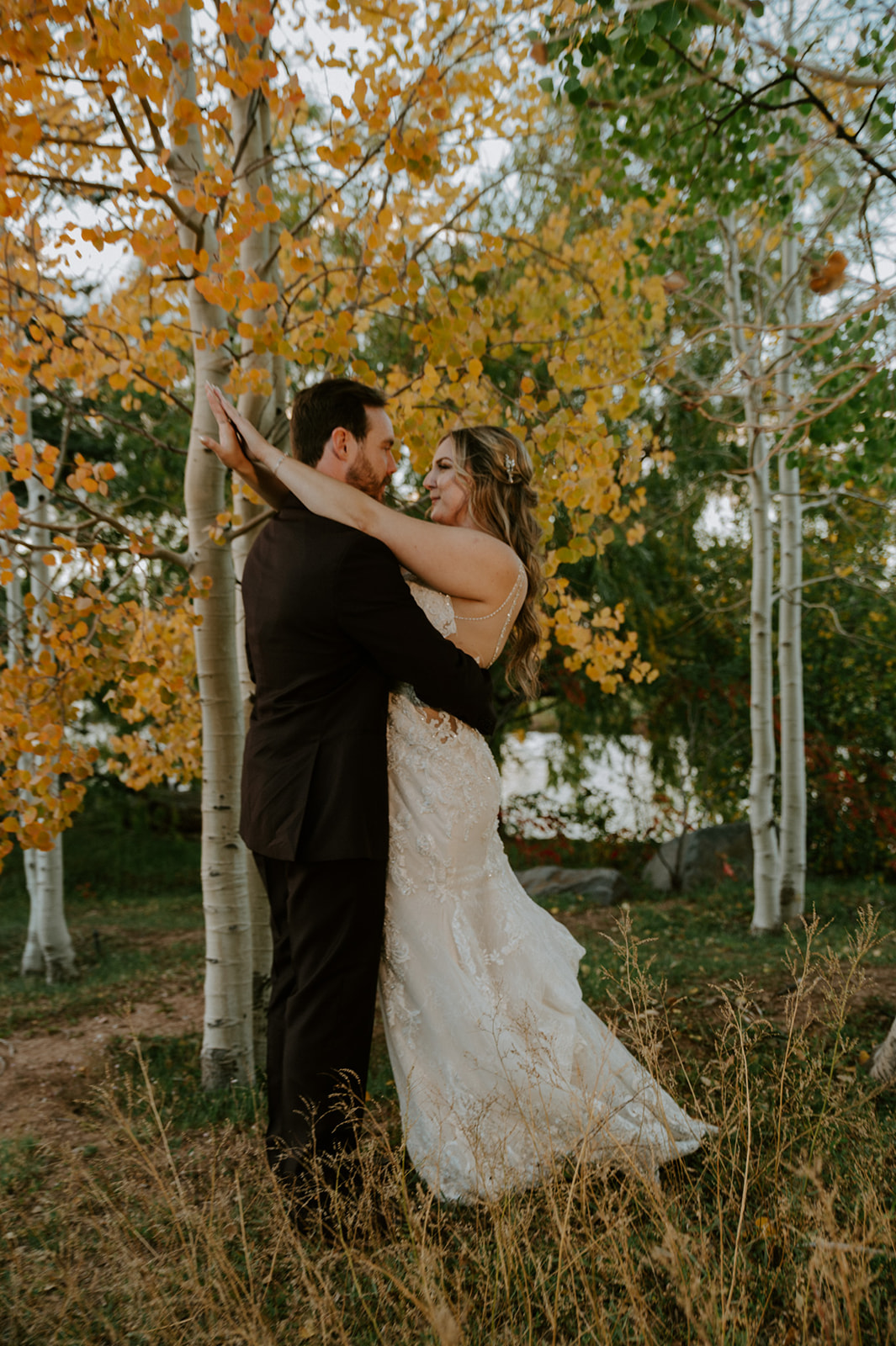 Newlyweds embrace among golden autumn aspens, surrounded by colorful fall foliage.
