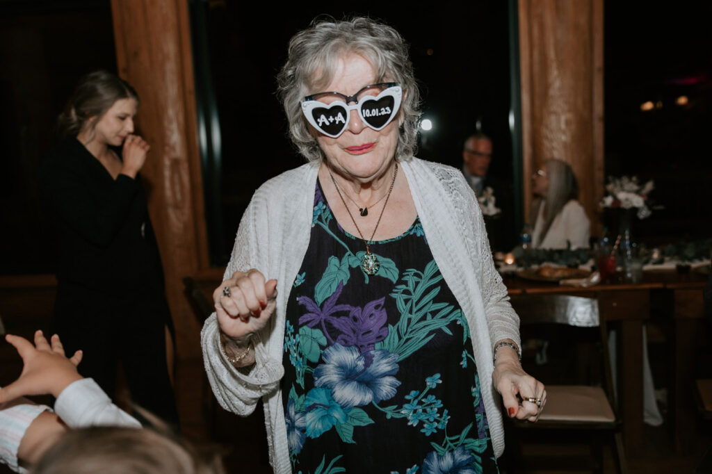 Grandmother wearing personalized wedding sunglasses smiles while dancing at the reception celebration.
