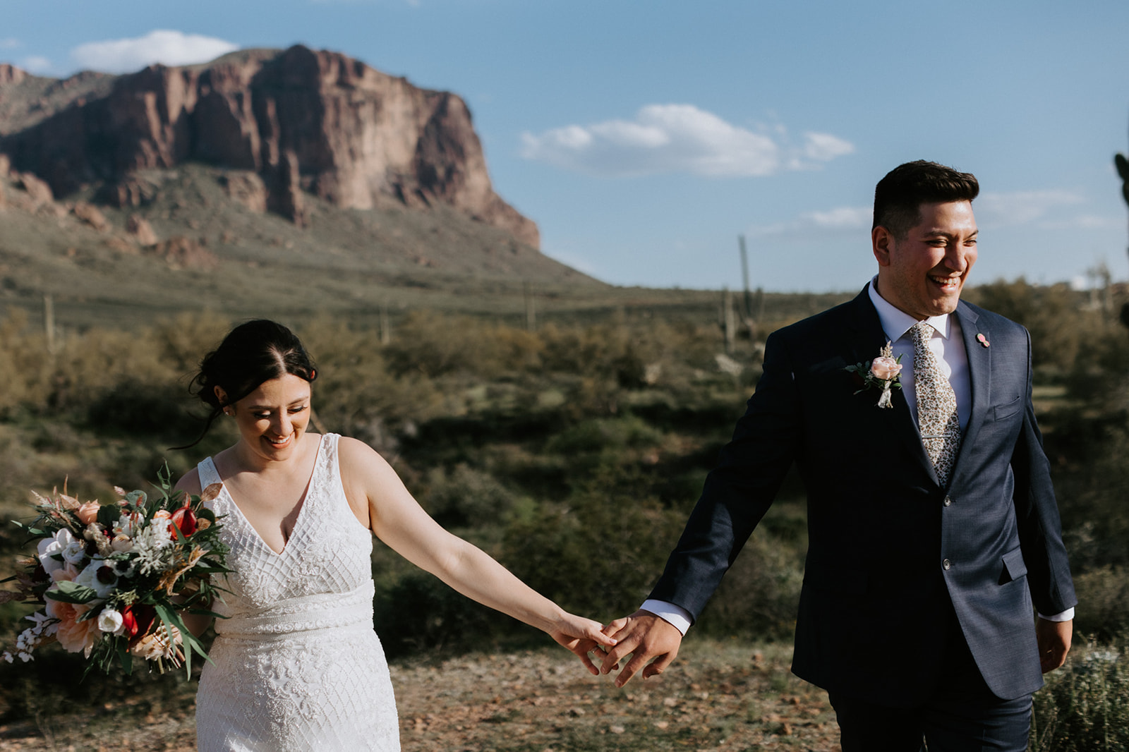Joyful newlyweds holding hands and laughing during their Arizona desert elopement portraits near mountain views.