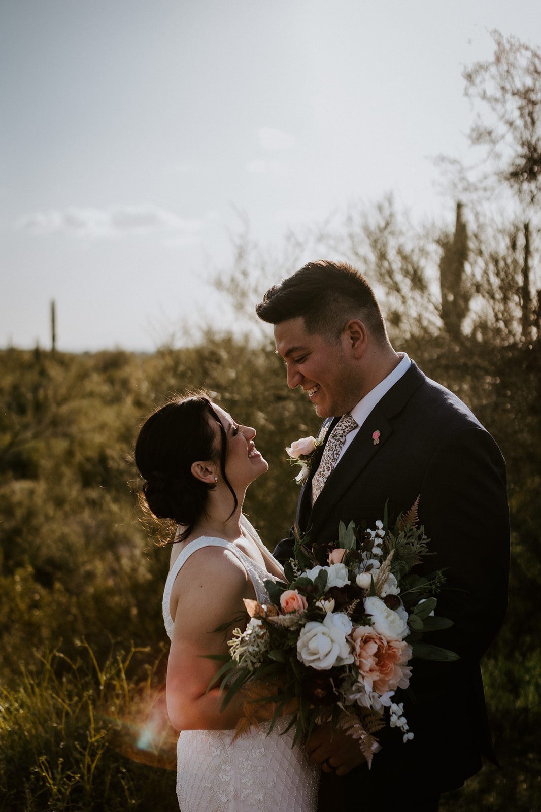 Romantic desert wedding portrait of bride and groom surrounded by saguaros and mountain views in Arizona.