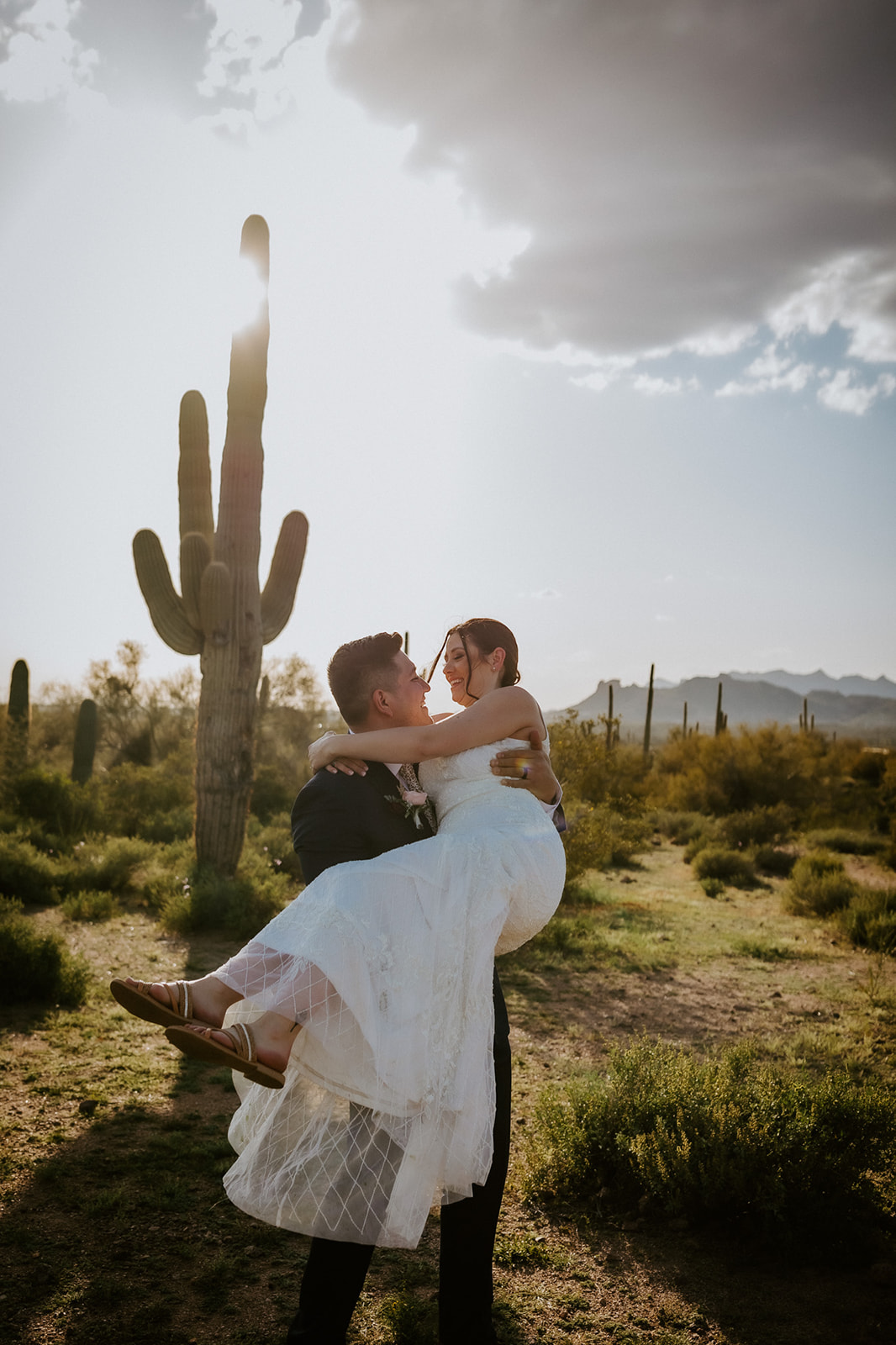 Groom lifting his bride beneath a saguaro cactus during a joyful moment eloping in Arizona
