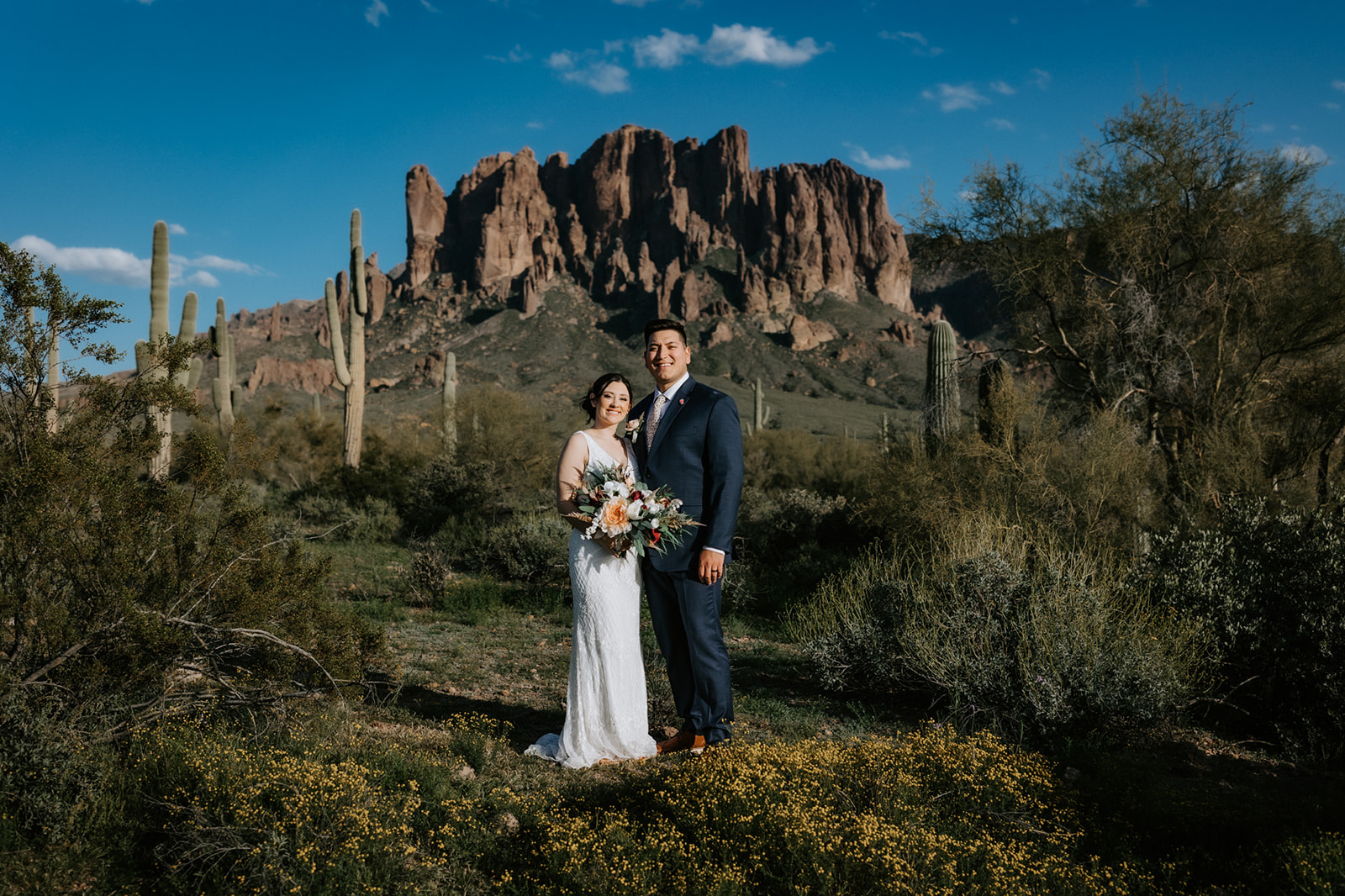Couple posing in front of the Superstition Mountains and Sonoran Desert landscape with blooming wildflowers
