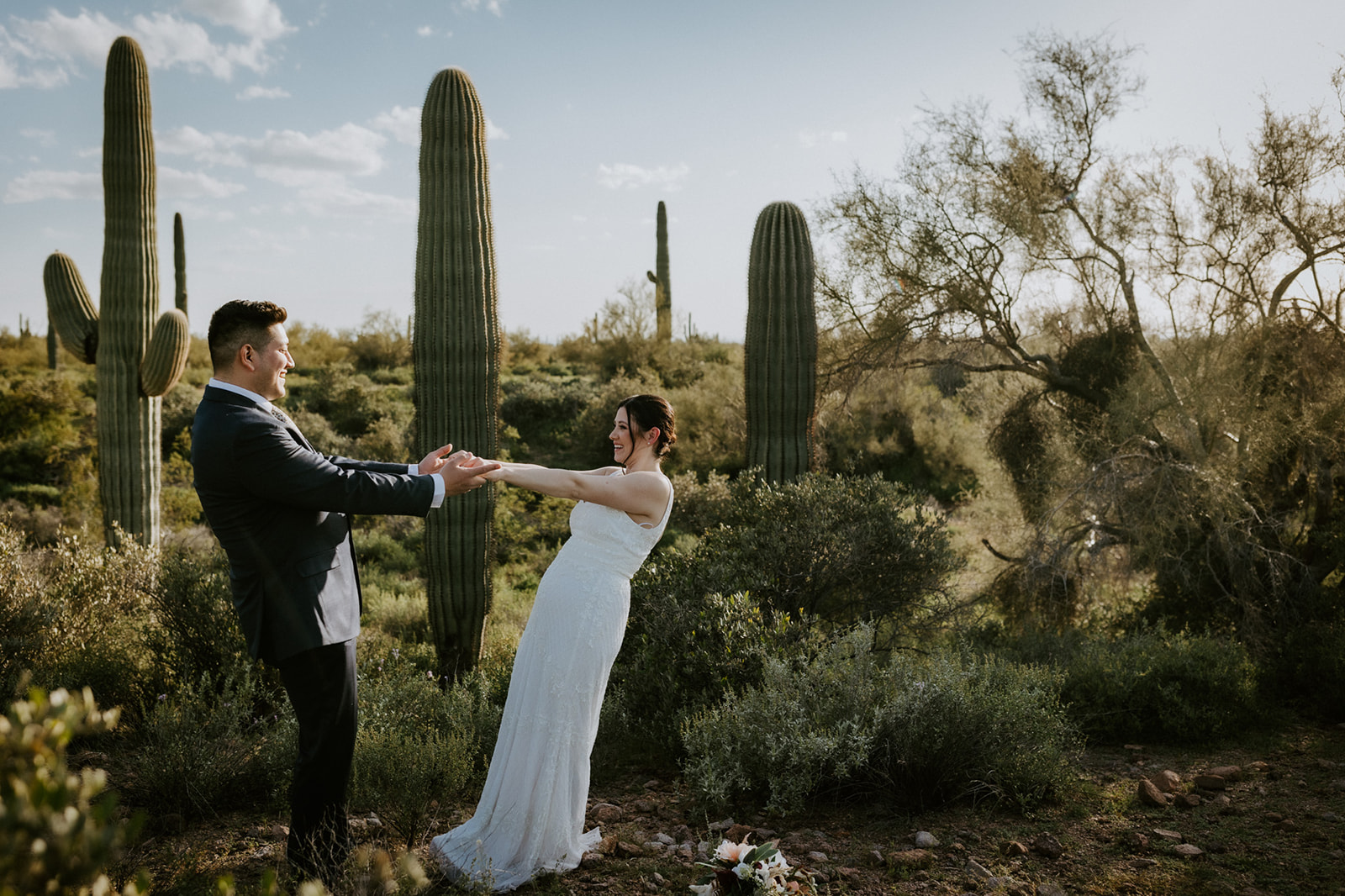 Playful bride and groom holding hands among towering saguaro cacti after eloping in Arizona.