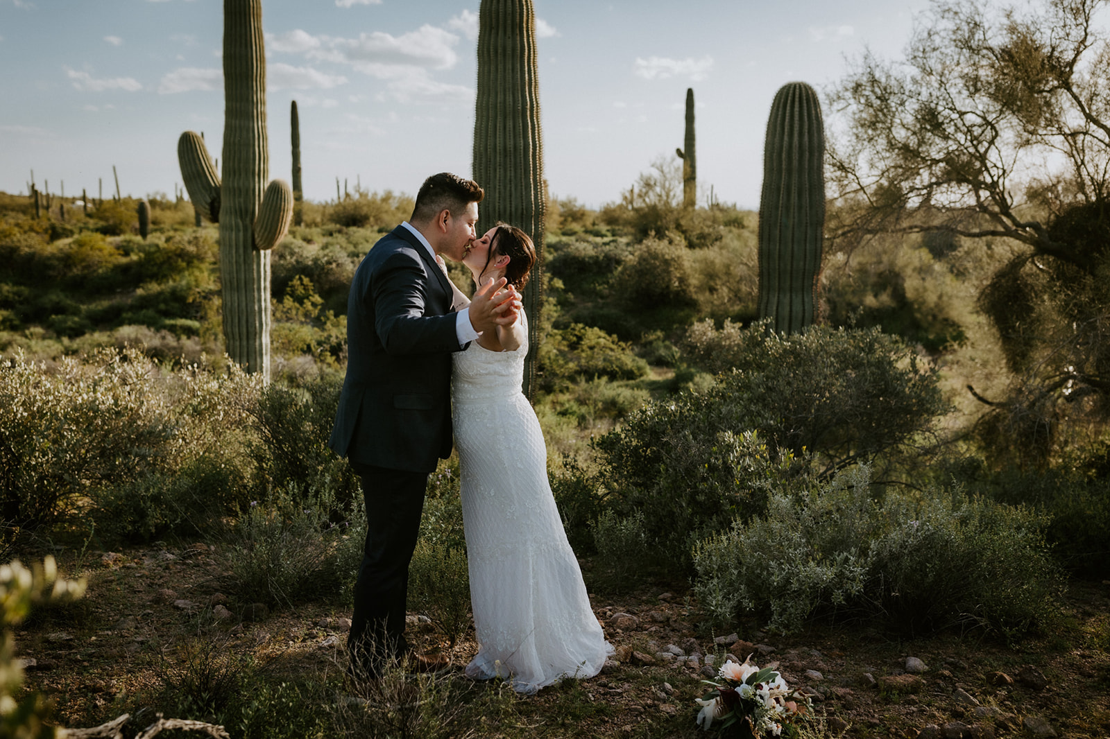 Couple kissing among towering saguaro cacti during an intimate day of eloping in Arizona desert wilderness
