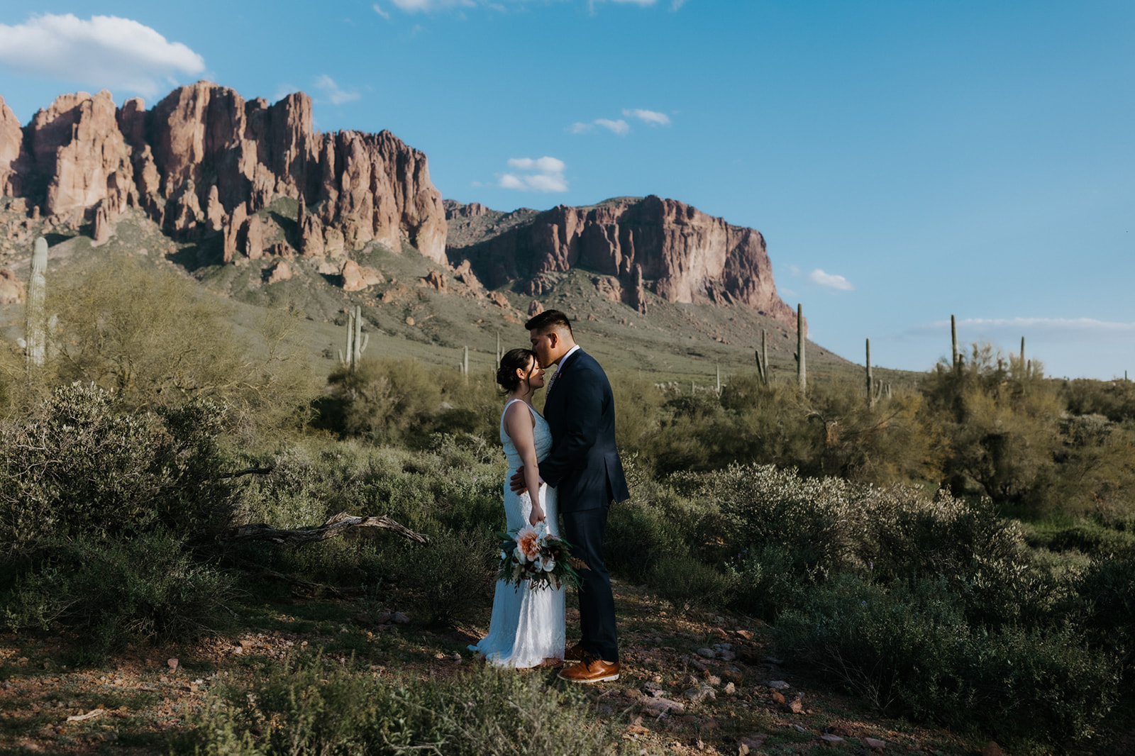 Bride and groom exchanging a kiss beneath mountain peaks while eloping in Arizona at golden hour
