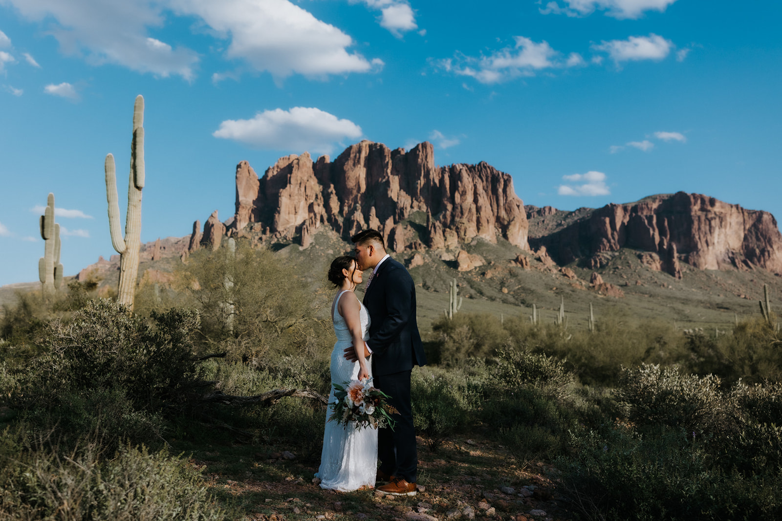 Newlywed couple sharing a kiss with the Superstition Mountains rising behind them in the Sonoran Desert landscape
