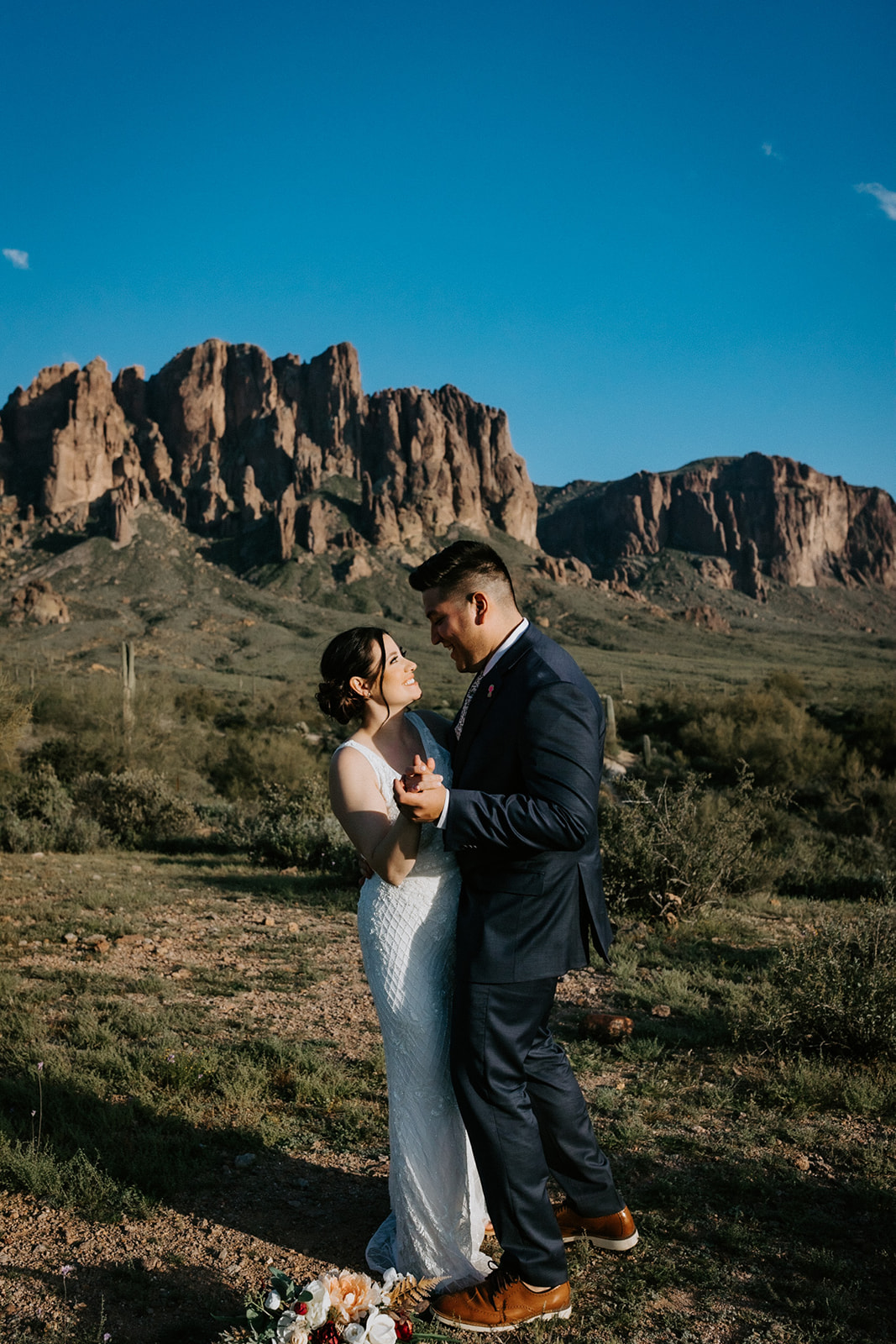 Newlyweds dancing together beneath dramatic desert mountains after eloping in Arizona.