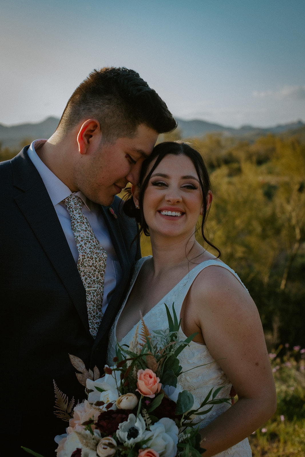Close-up portrait of newlyweds smiling together while holding a colorful desert-inspired wedding bouquet
