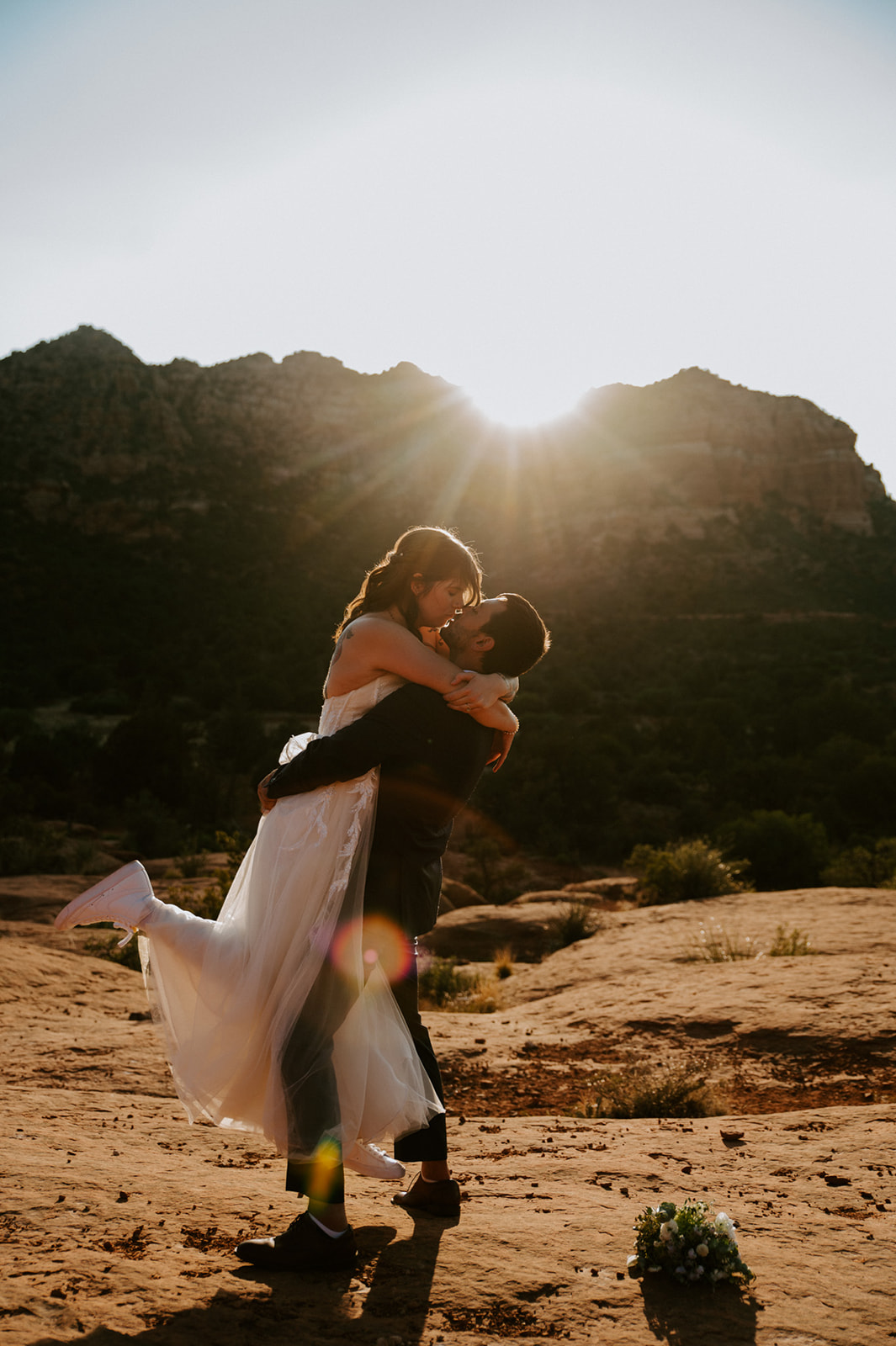 Groom lifting his bride on Sedona red rocks as the sun sets behind the canyon landscape
