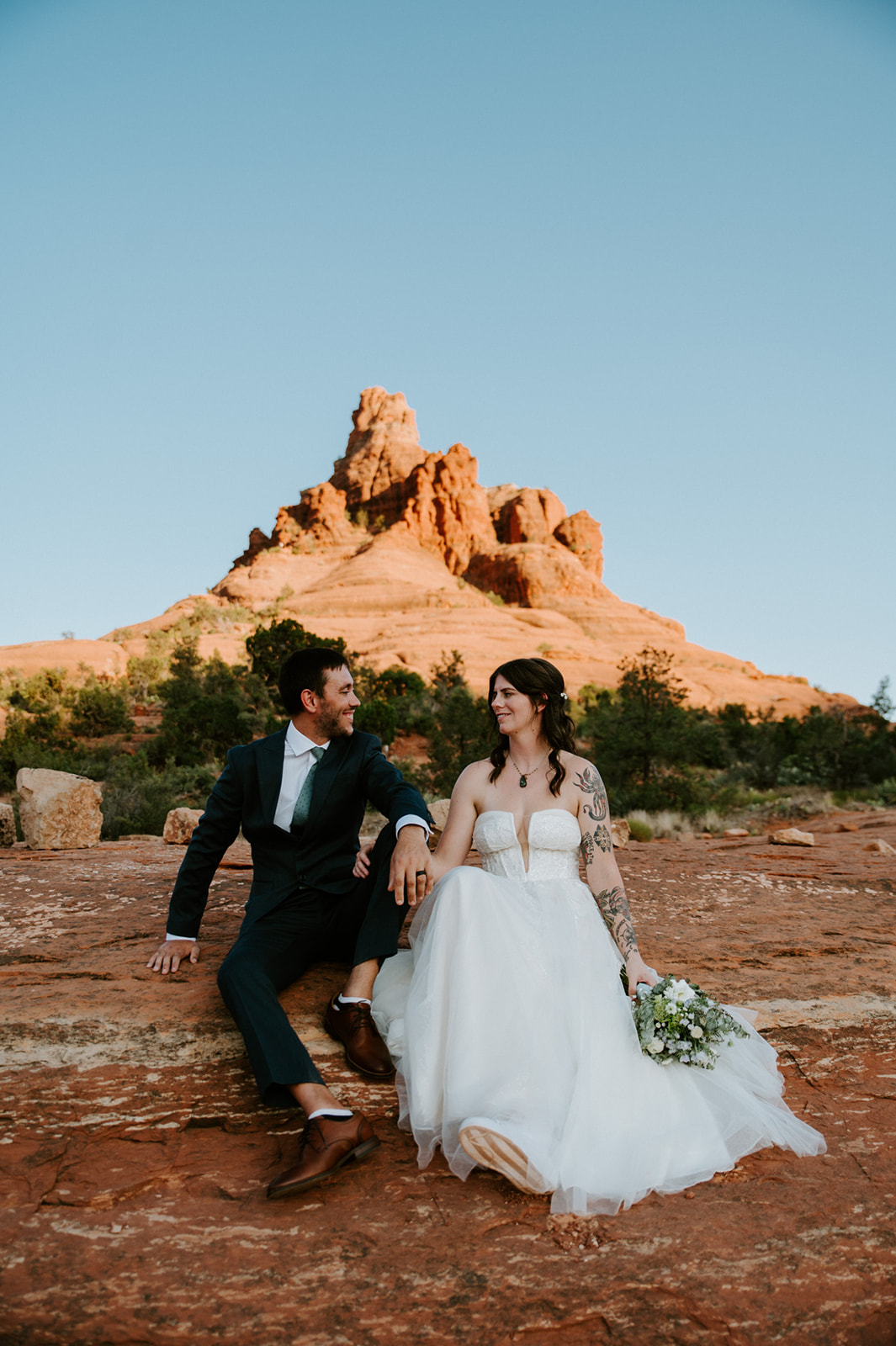 Newlywed couple seated on red rock formations in Sedona during a scenic day of eloping in Arizona
