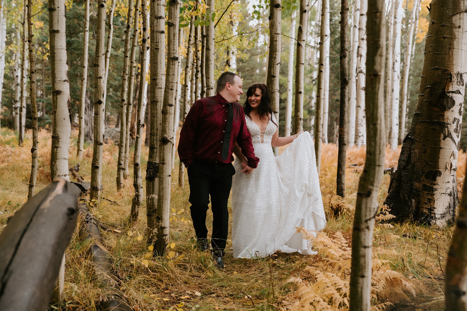 Bride and groom walking hand in hand through colorful aspens at one of Arizona wedding locations.